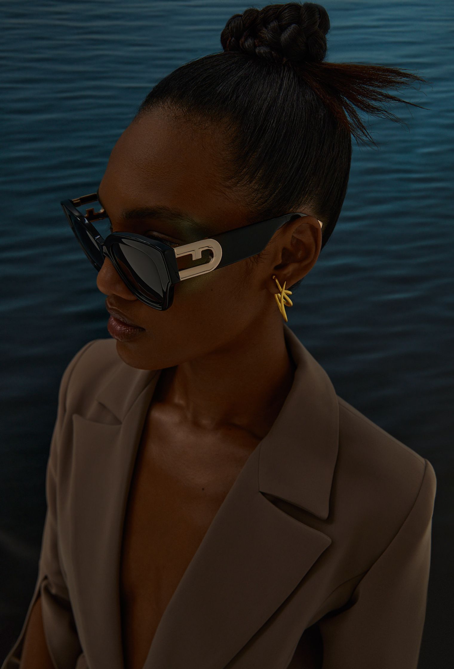 a woman wearing sunglasses and a blazer in front of a body of water