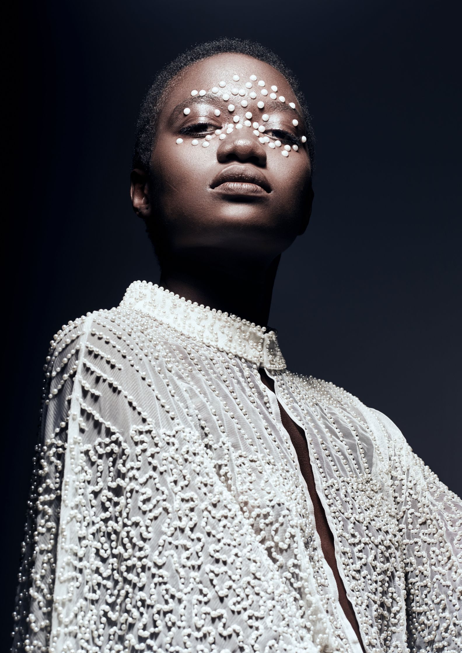 Model wearing pearl-adorned clothing with face embellishments, reflecting opulence and sophisticated beauty