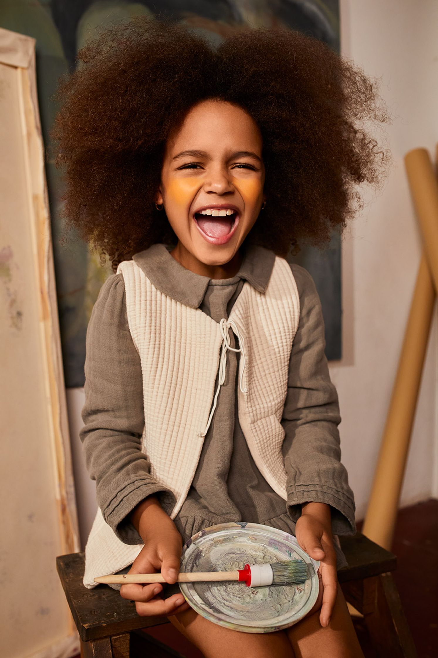 a little girl with afro hair sitting on a chair holding a plate