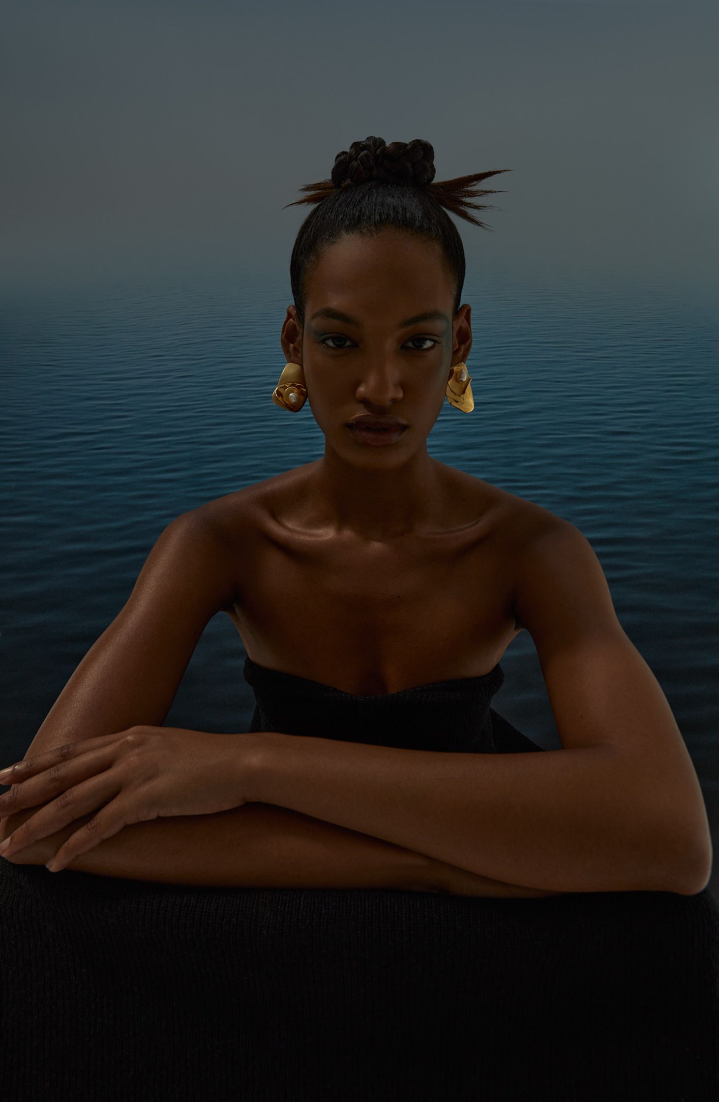 a woman in a black dress sitting on a bench in front of a body of water