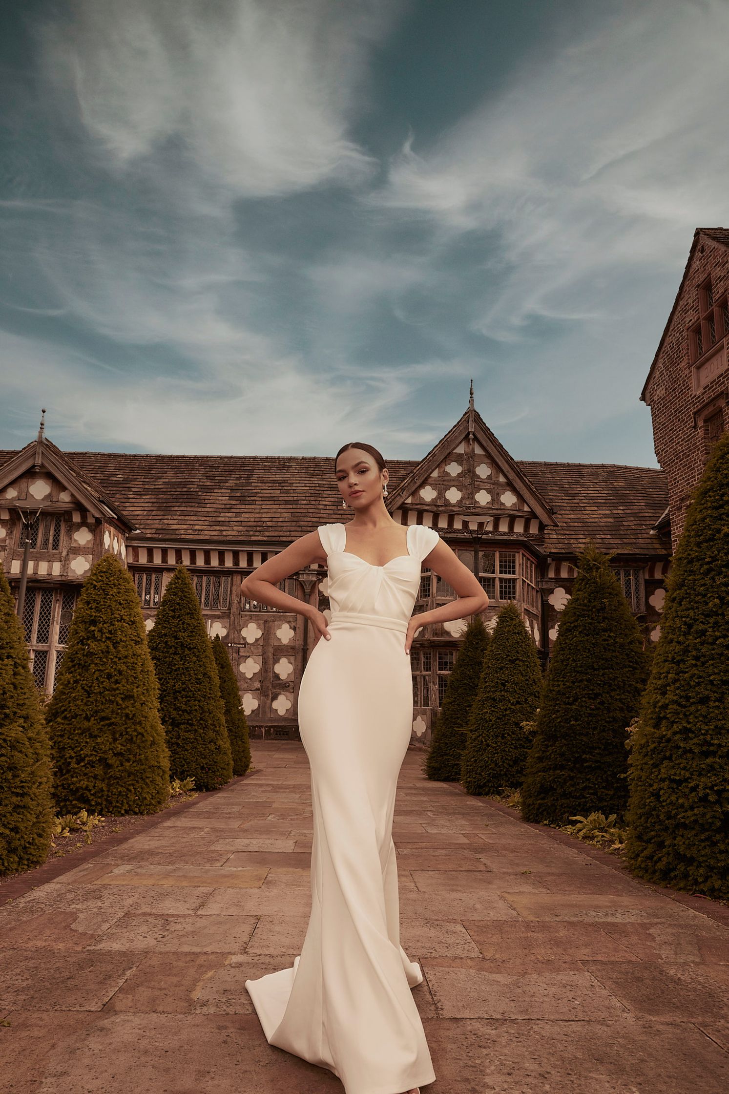 a bride in a white wedding dress posing in front of a mansion