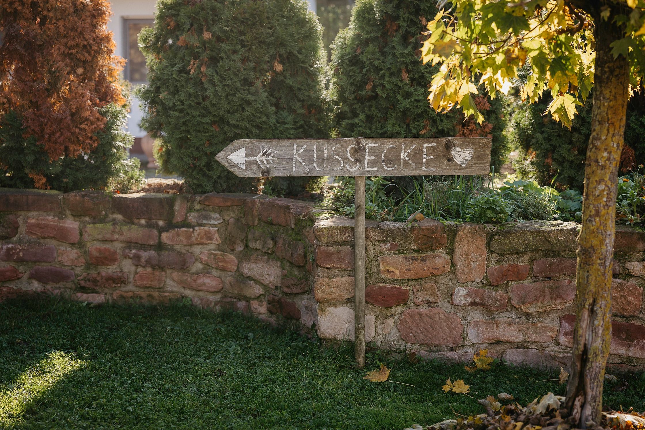 ein Schild mit der aufschrift Kussecke vor einer Steinmauer mit einem Baum im Hintergrund