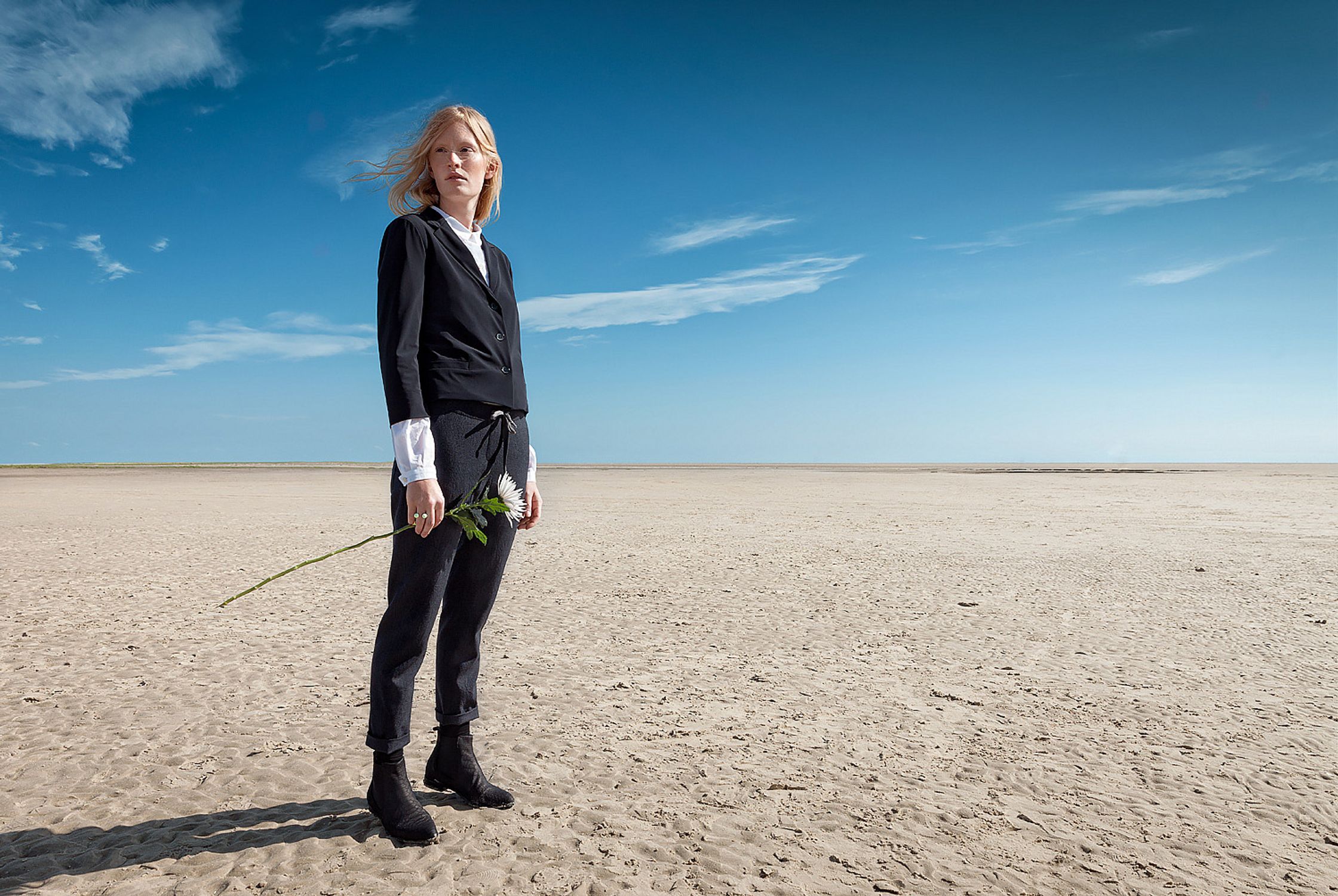 a woman standing on a deserted beach with a flower in her hand retouche advertising campaign