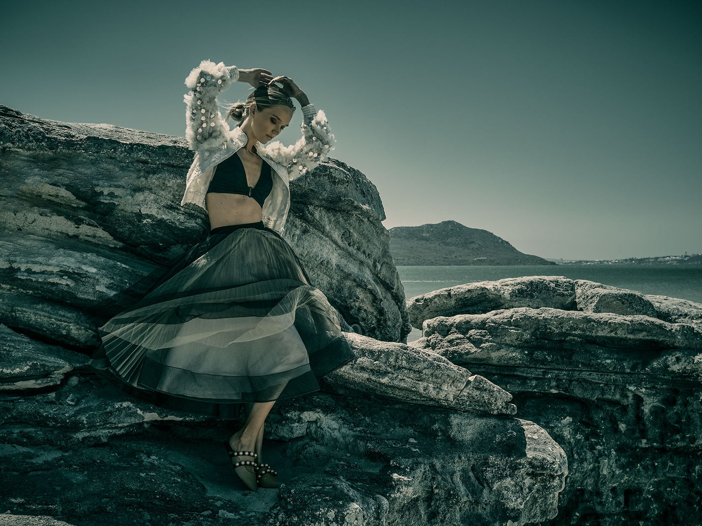 a woman is posing on a rock near the ocean