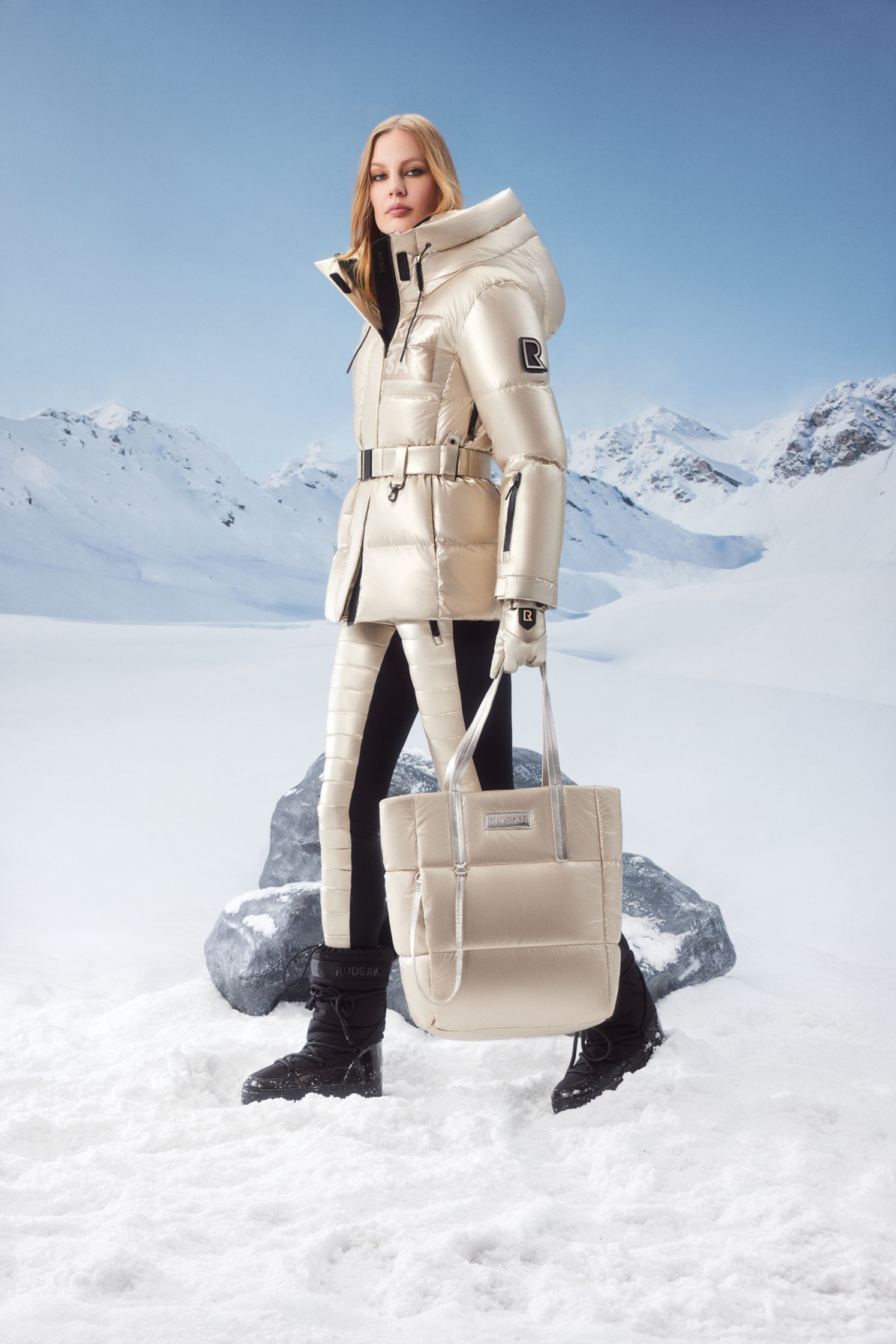 a woman in a down jacket walking in the snow with a bag