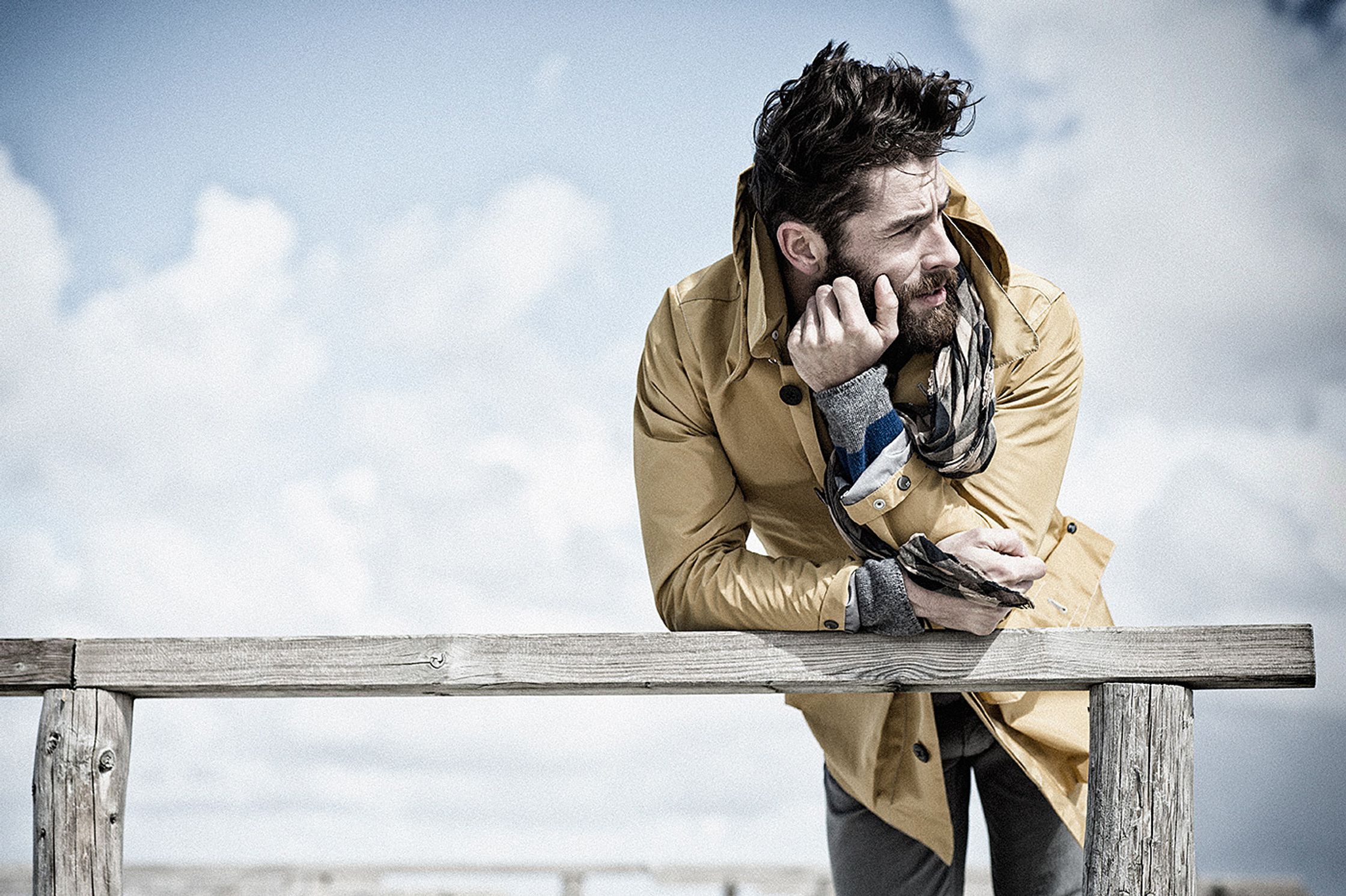 a man in a yellow coat leaning on a railing while talking on his cell phone Bildbearbeitung image campaign