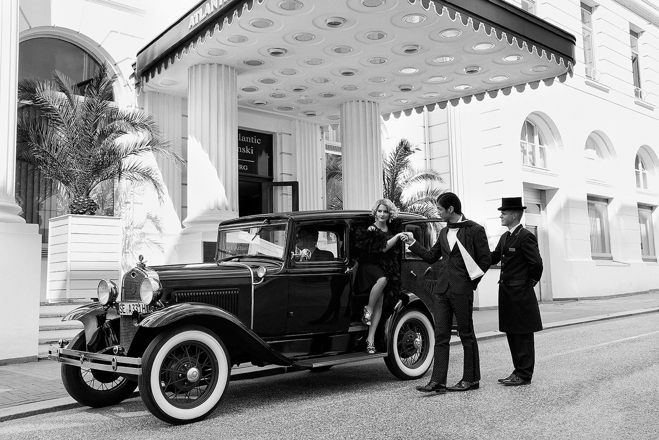 two men standing next to an antique car in front of a hotel advertising retouch hamburg