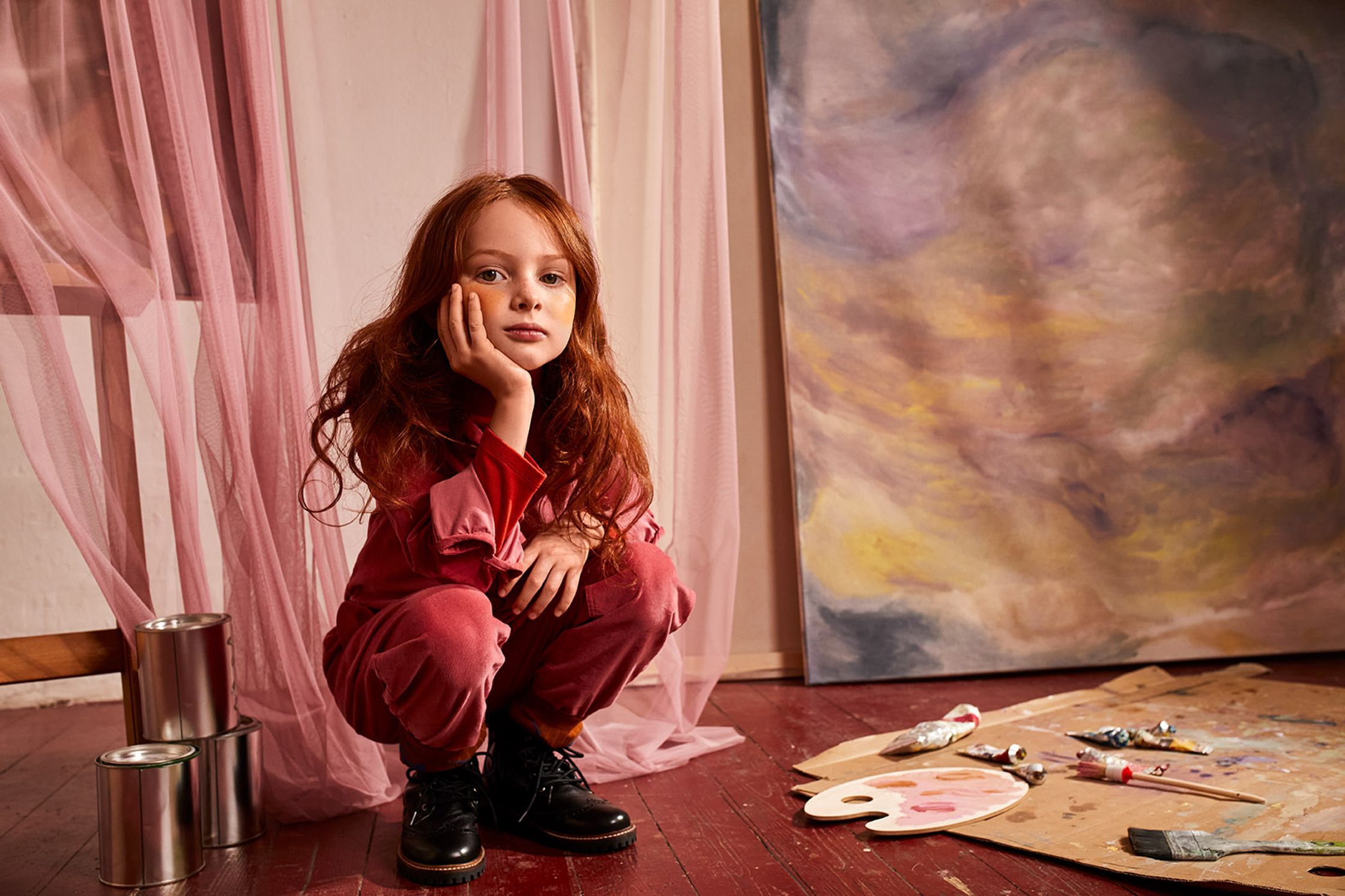 a girl in a pink jumpsuit sitting on the floor in front of a painting