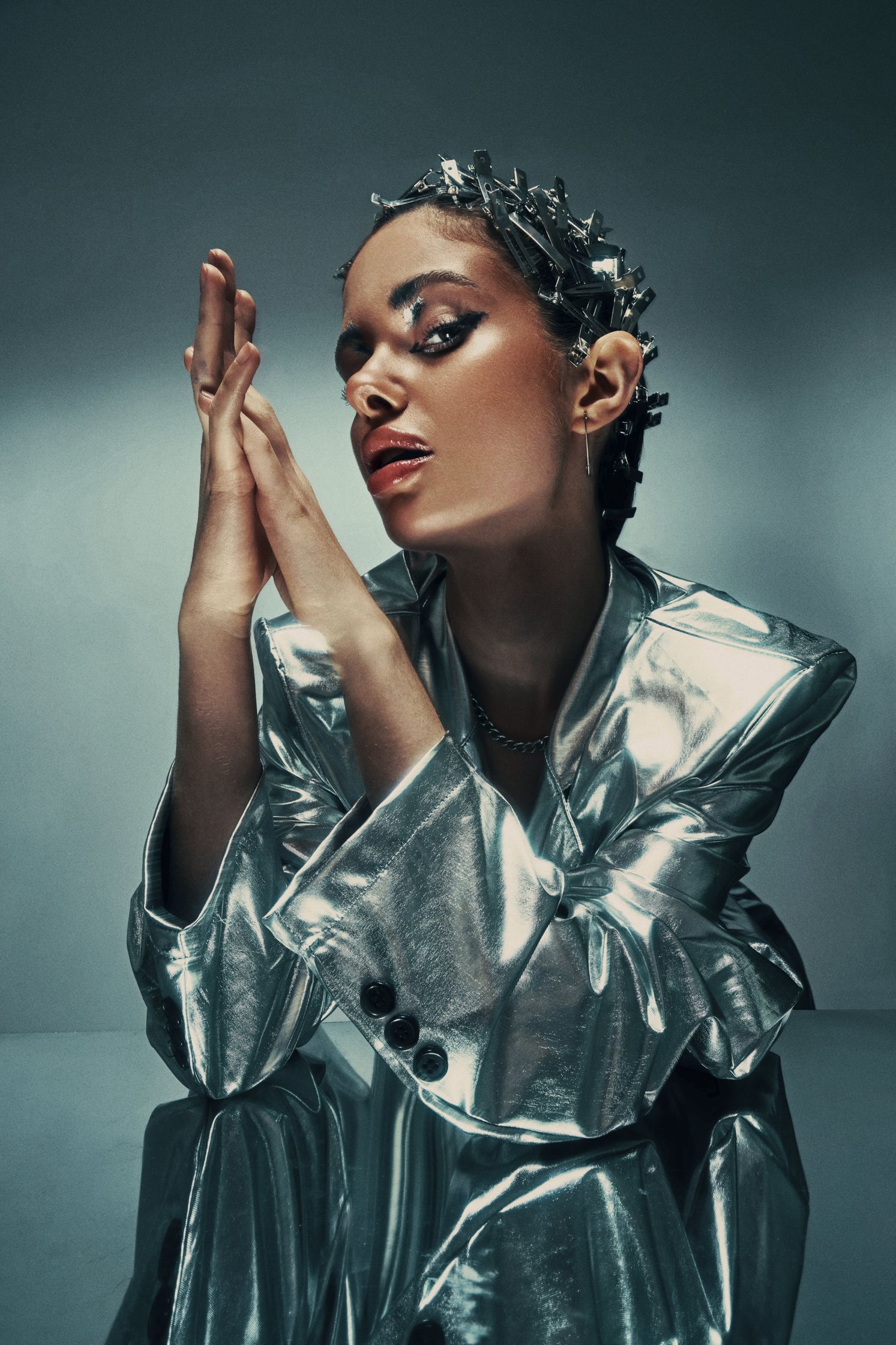 Close-up portrait of Monique Bourscheid in a silver metallic jacket with intricate hair clips and bold makeup.