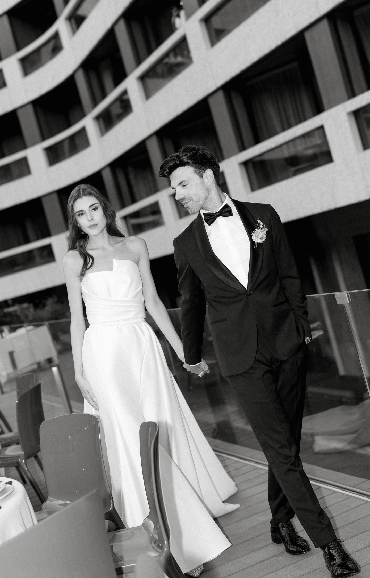 black and white photo of Vivienne Oesch and Vasilis Zorba as bride and groom walking on the terrace of the FIVE HOTEL ZURICH. Bridal glam makeup. Hair and makeup by Denise Dedich.