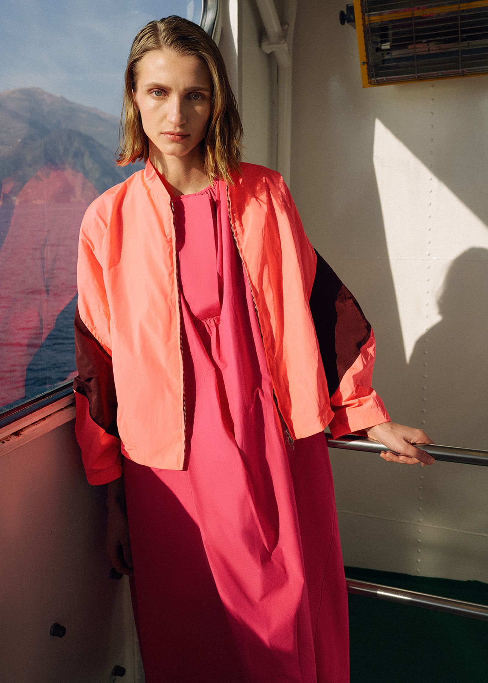 a woman in a pink dress standing on the deck of a boat