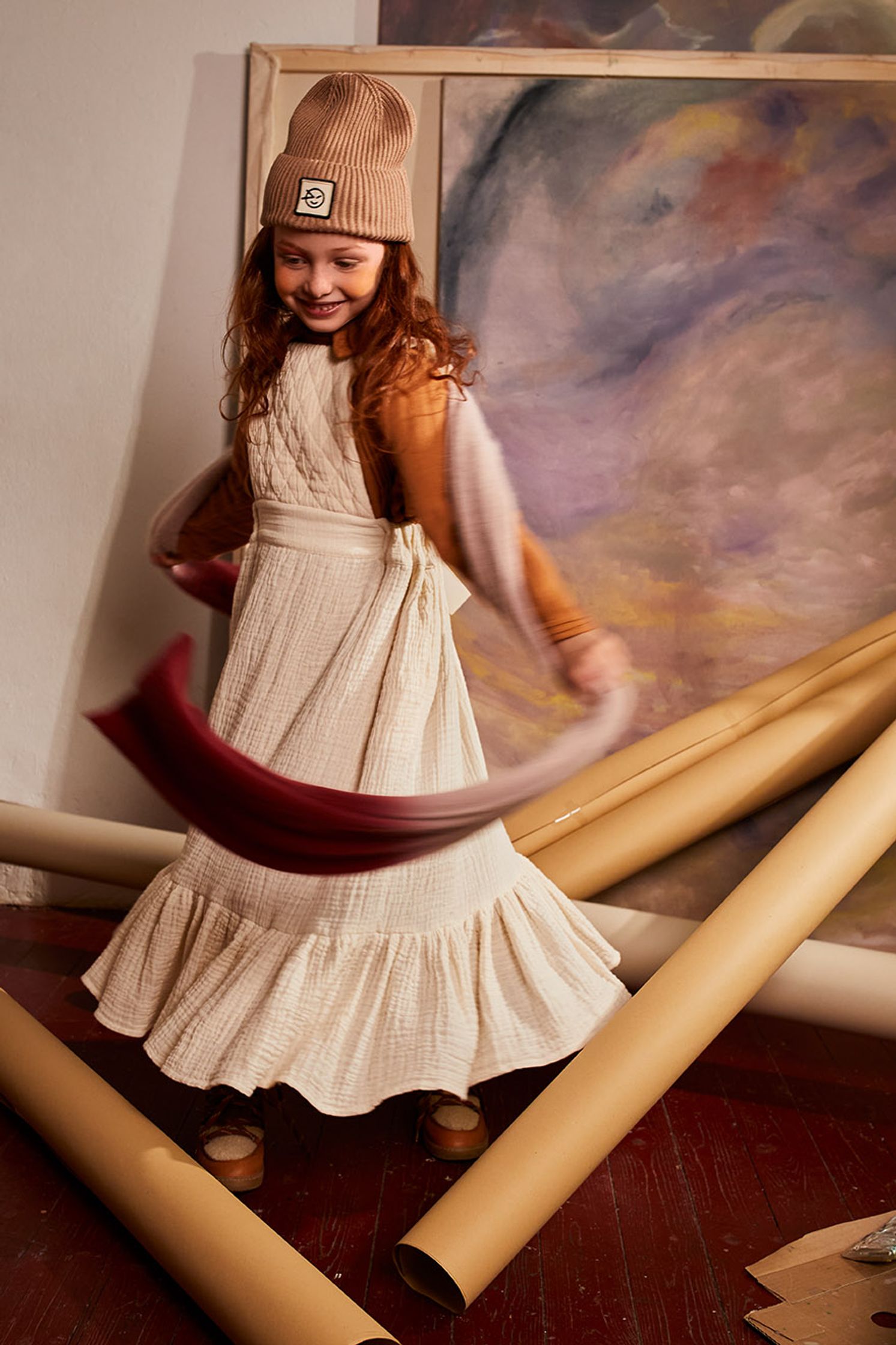 a little girl in a white dress and hat playing with rolls of paper