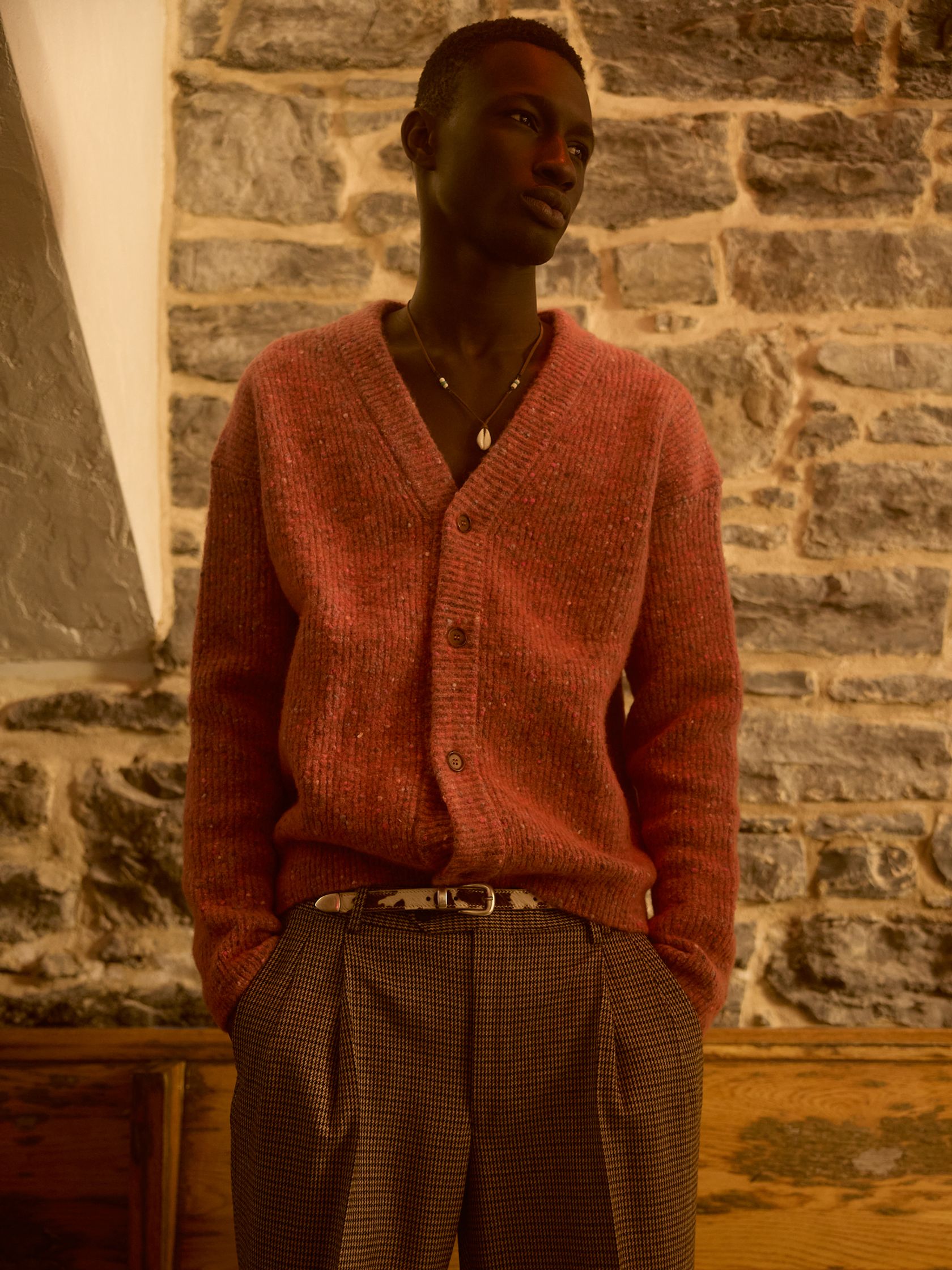 a man in a pink sweater and pants standing in front of a stone wall