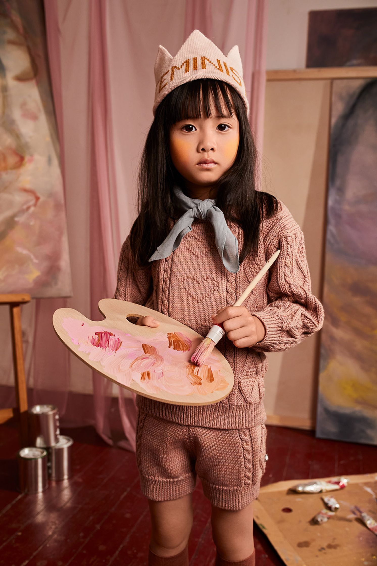 a little girl in a pink hat holding a palette