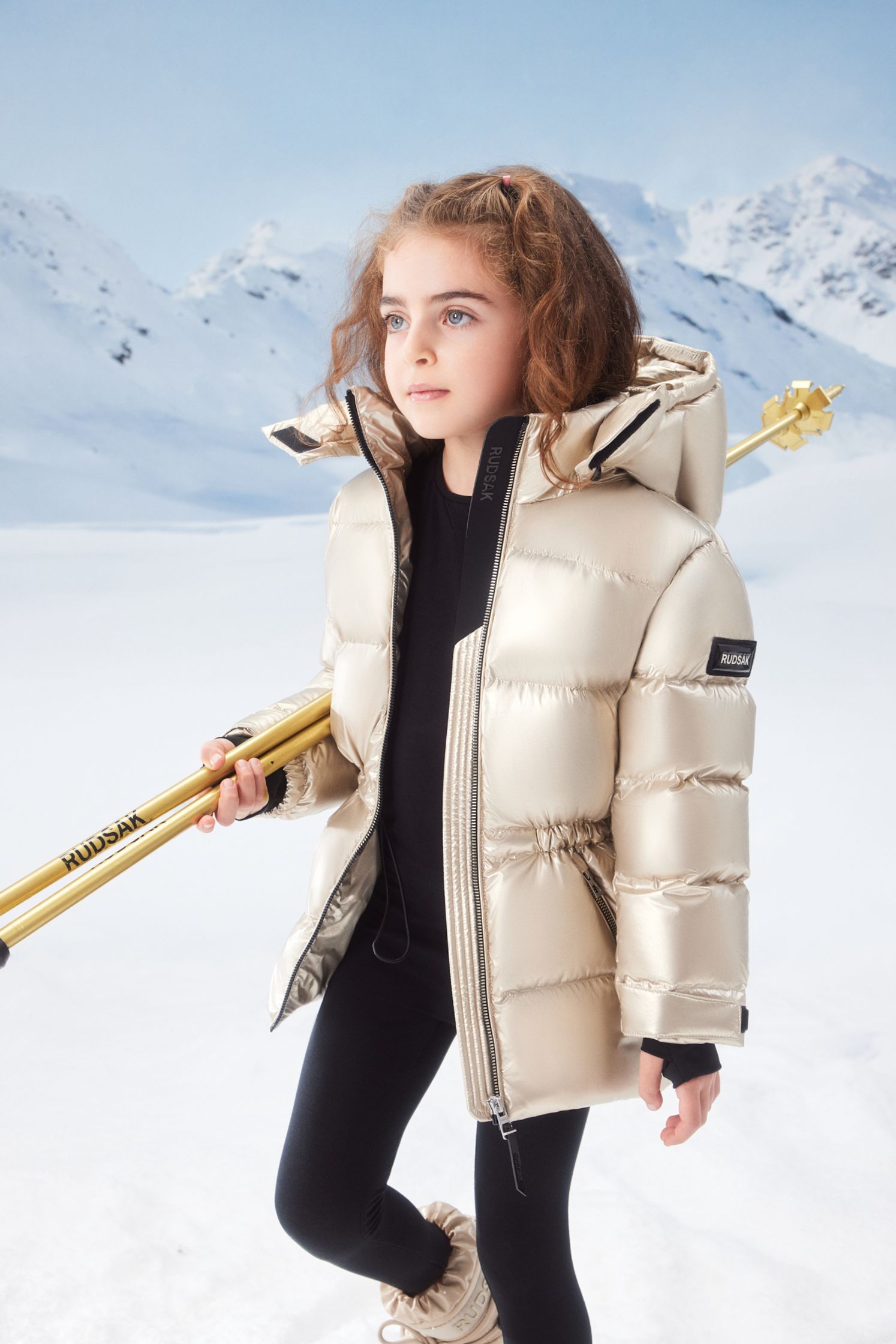 a girl in a gold puffer jacket holding skis in the snow