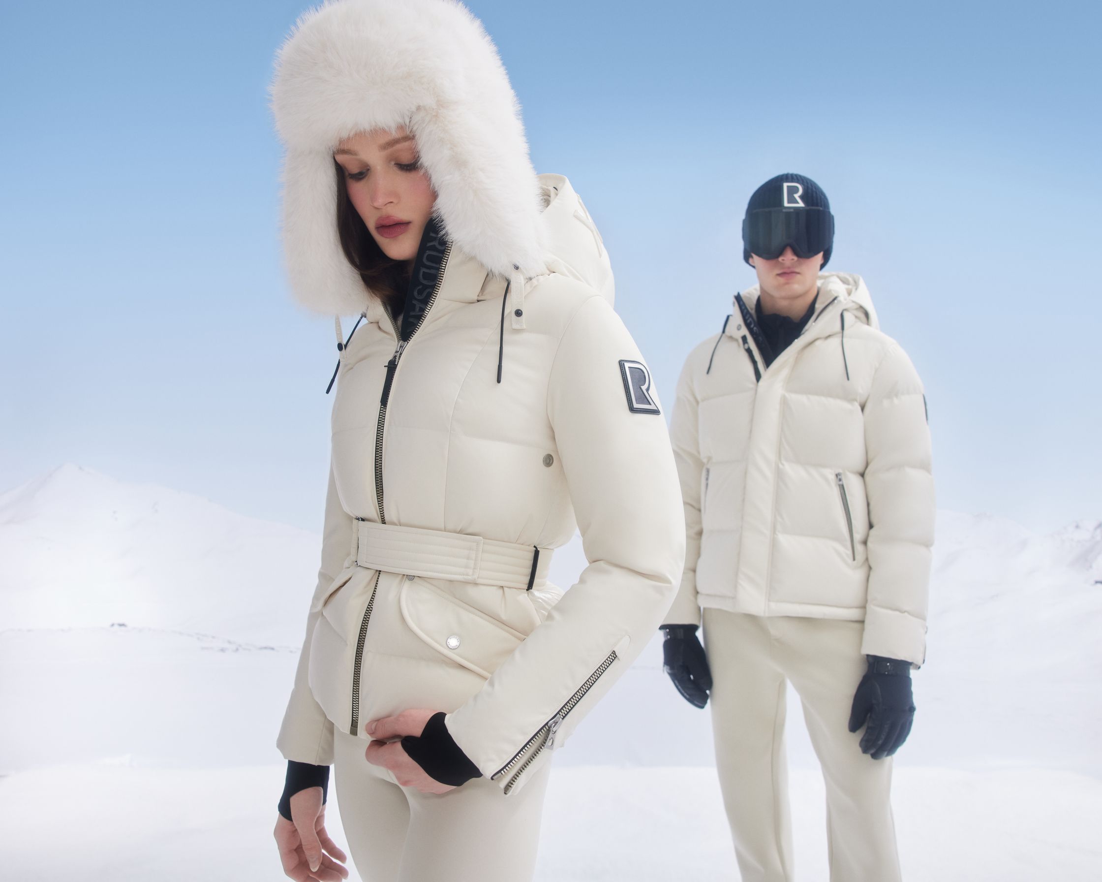 a man and woman dressed in white down jackets and fur hats