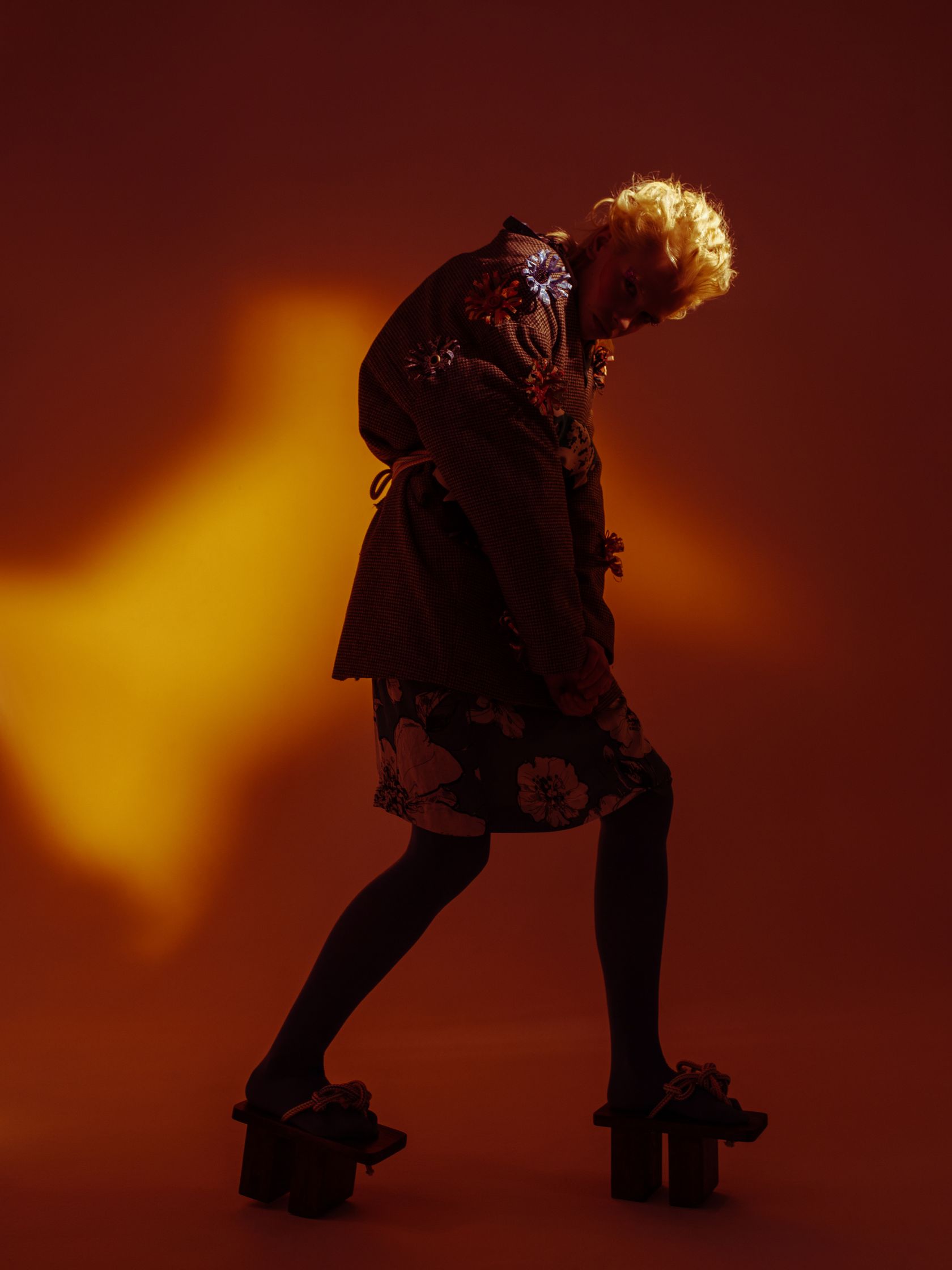 a woman wearing a jacket and boots is standing in front of an orange light