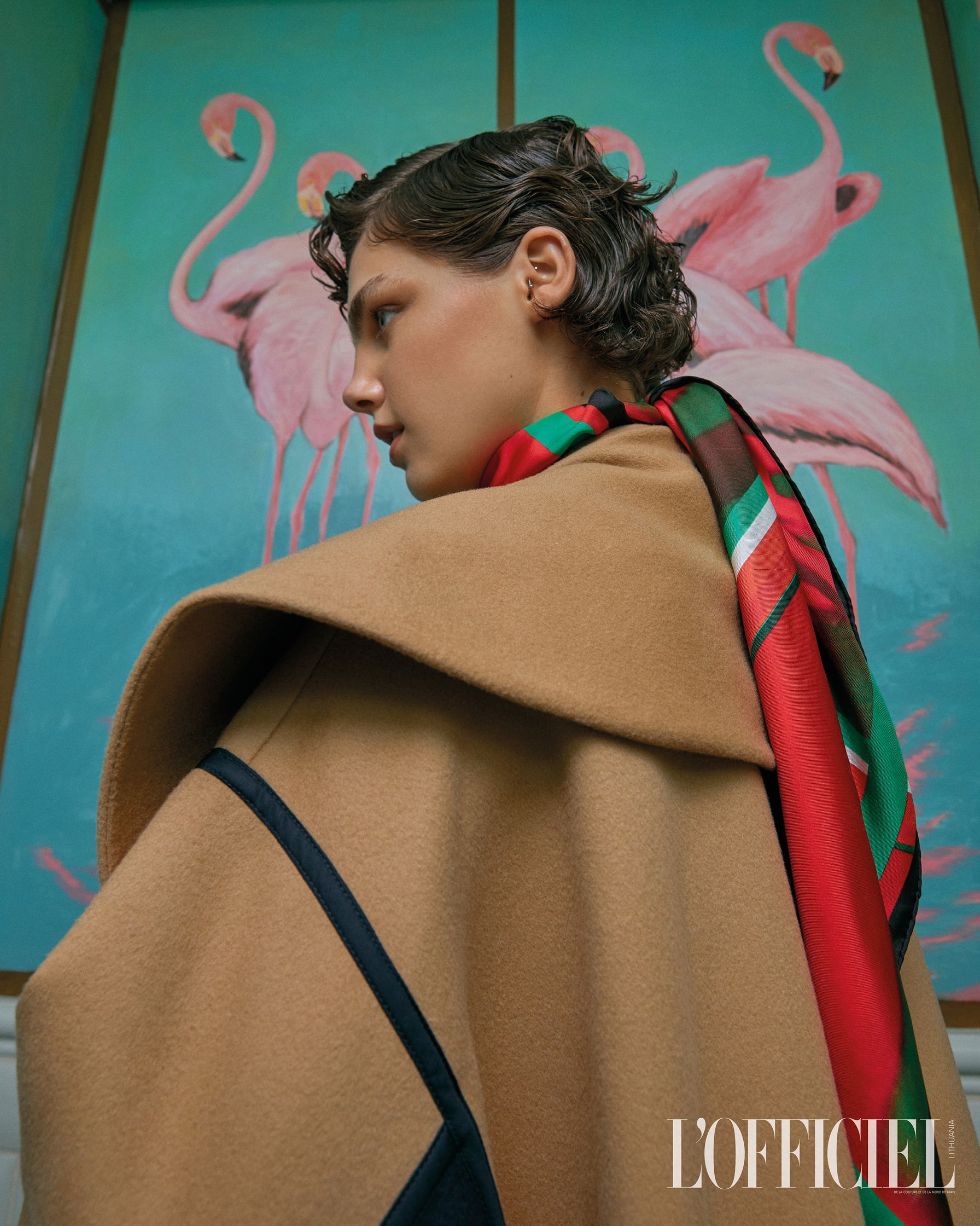 a woman in a tan coat is standing in front of flamingos