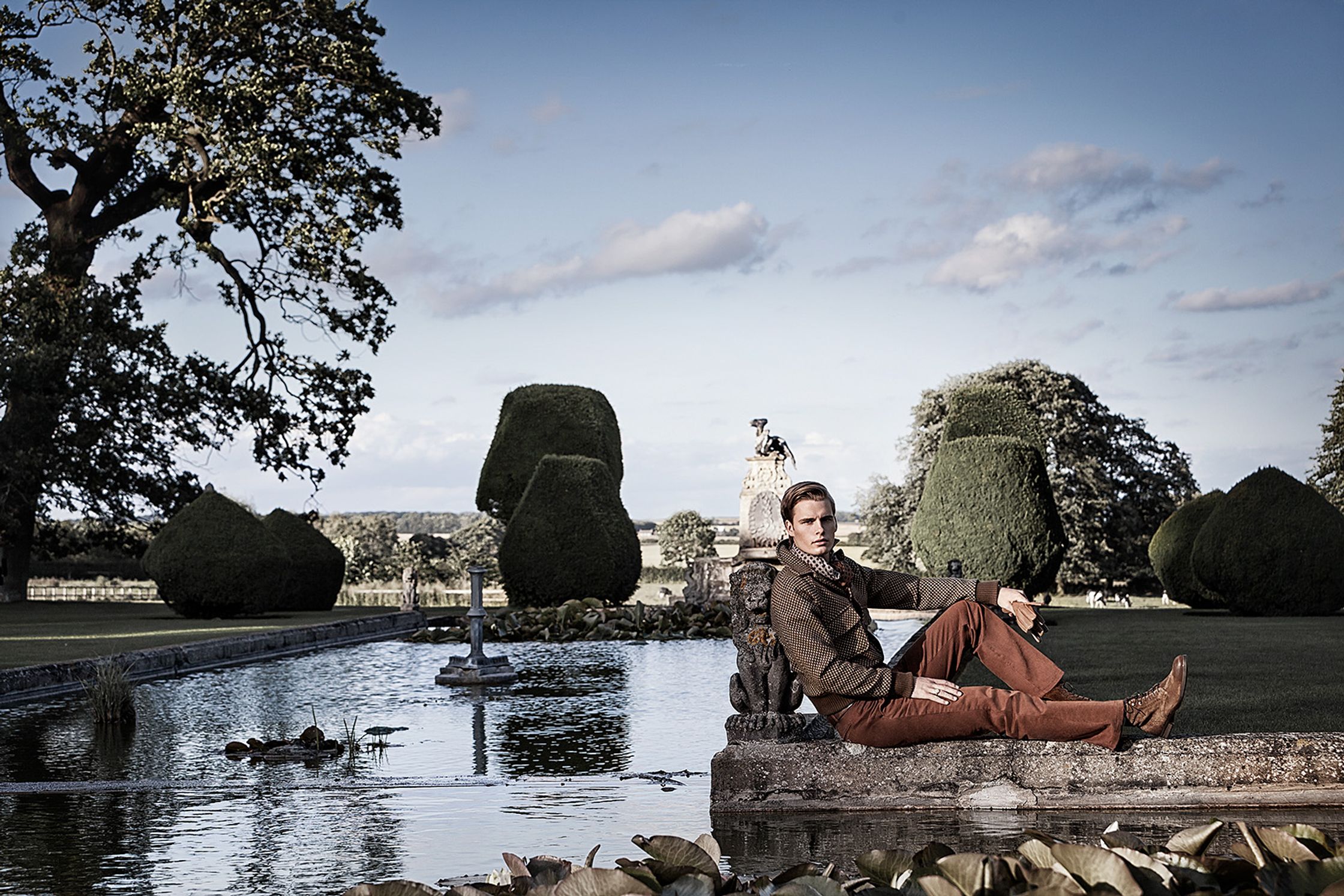 a man sitting on a rock in front of a pond creative post production