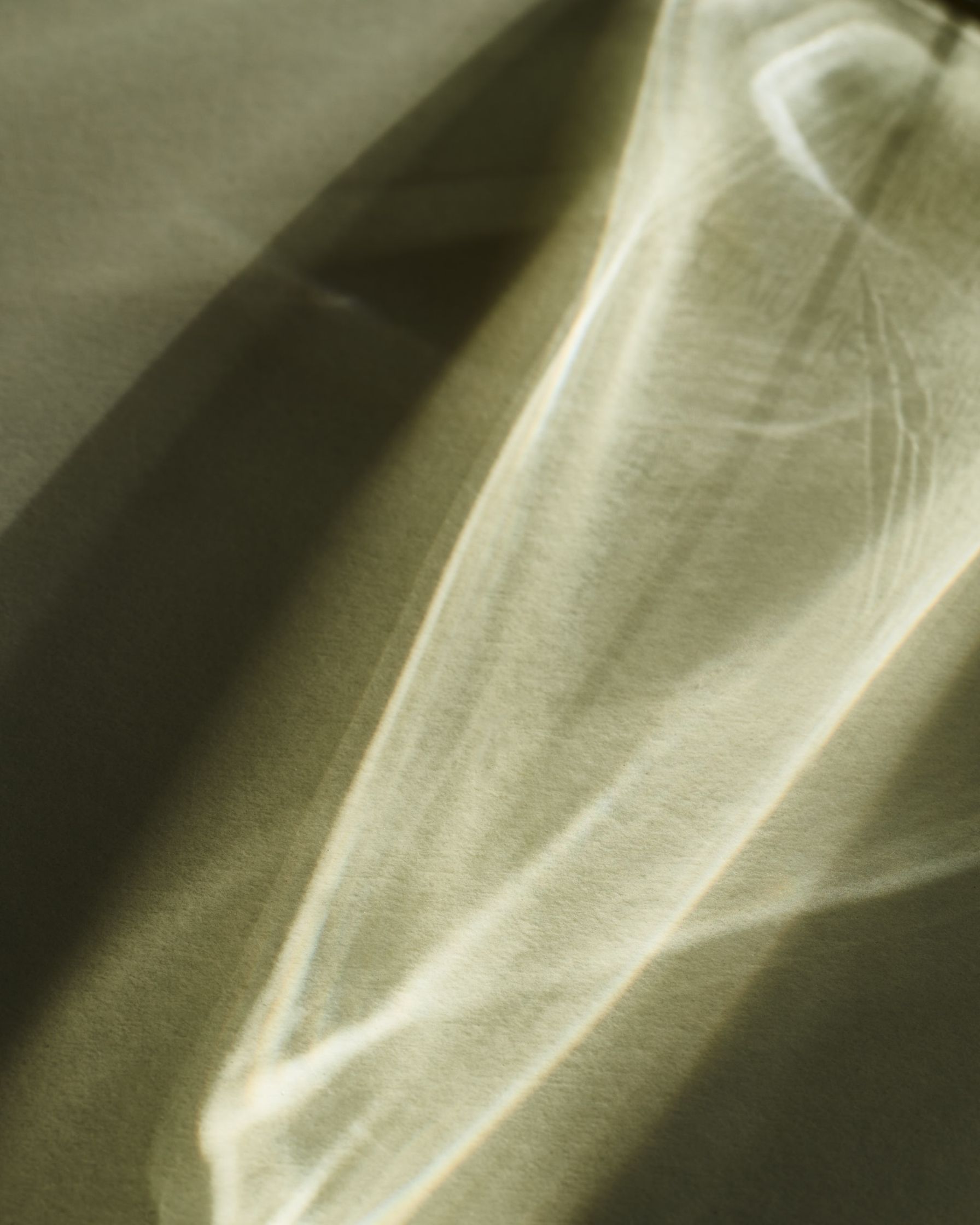 Abstract shot of the Calvin Klein perfume bottle's light reflection, creating soft, flowing lines on a neutral background.