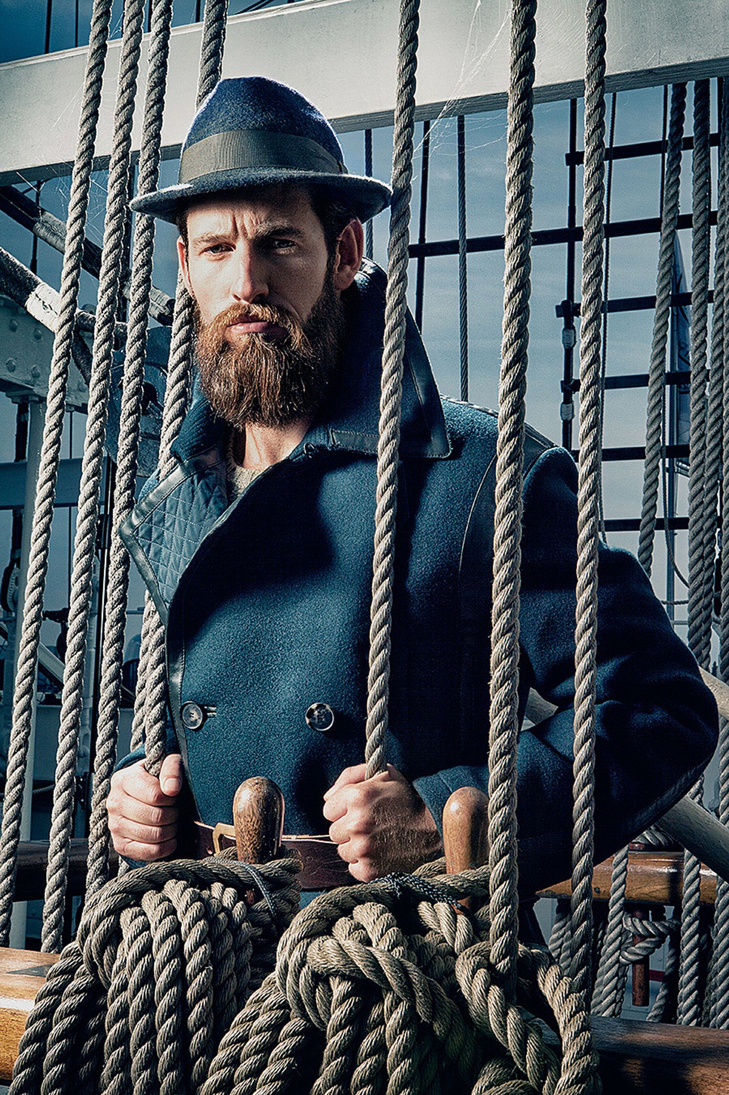 a bearded man wearing a hat and coat on a ship Creative Retouching Hamburg