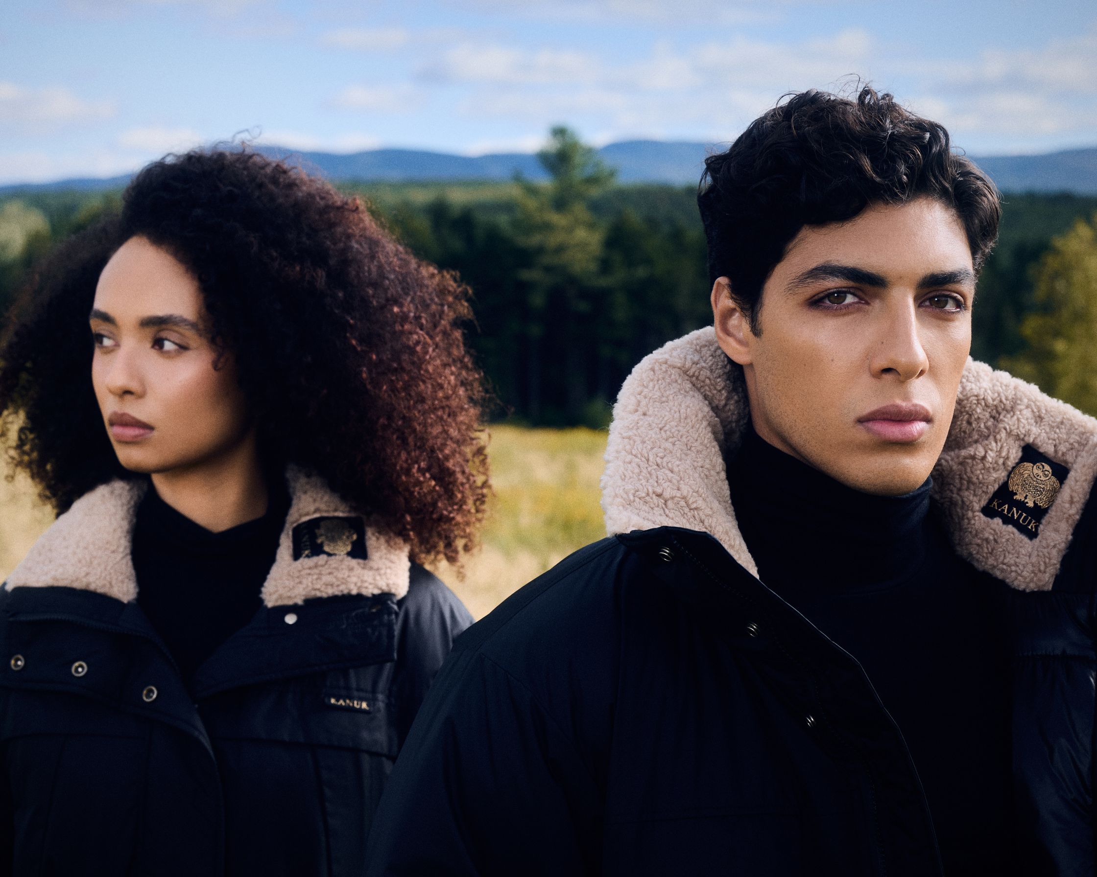 a man and a woman in black jackets standing in a field