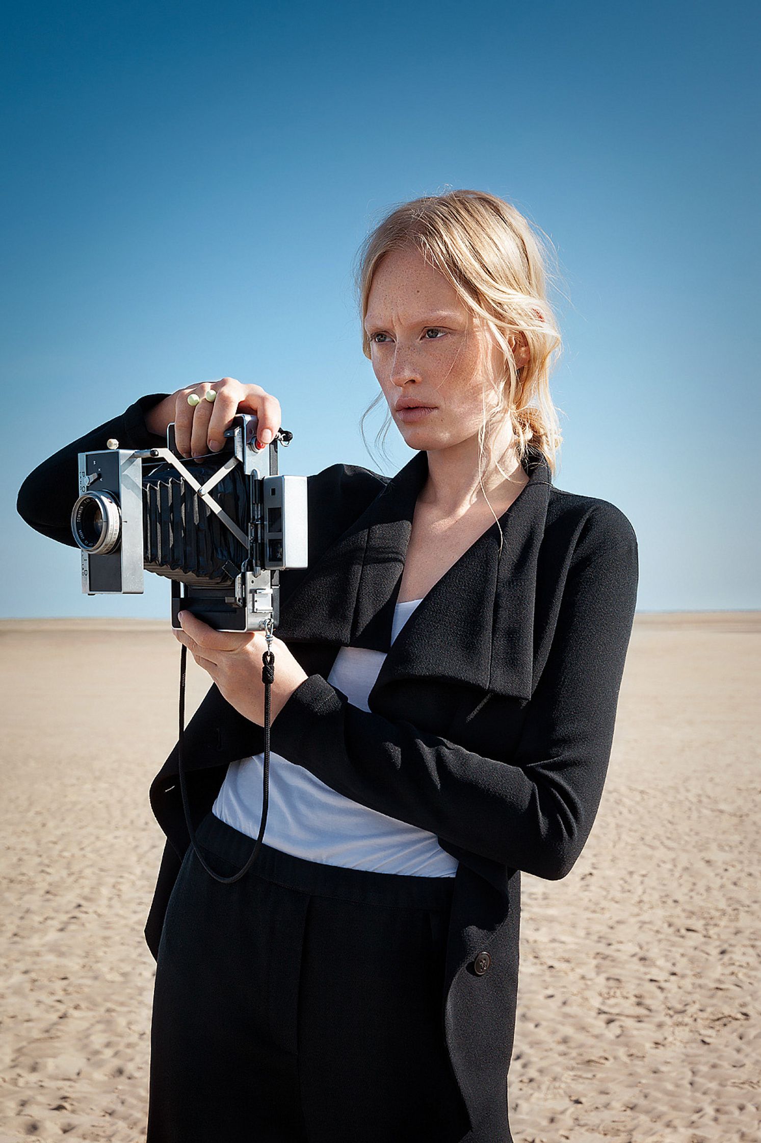 a woman holding a camera on the beach retouche advertising campaign