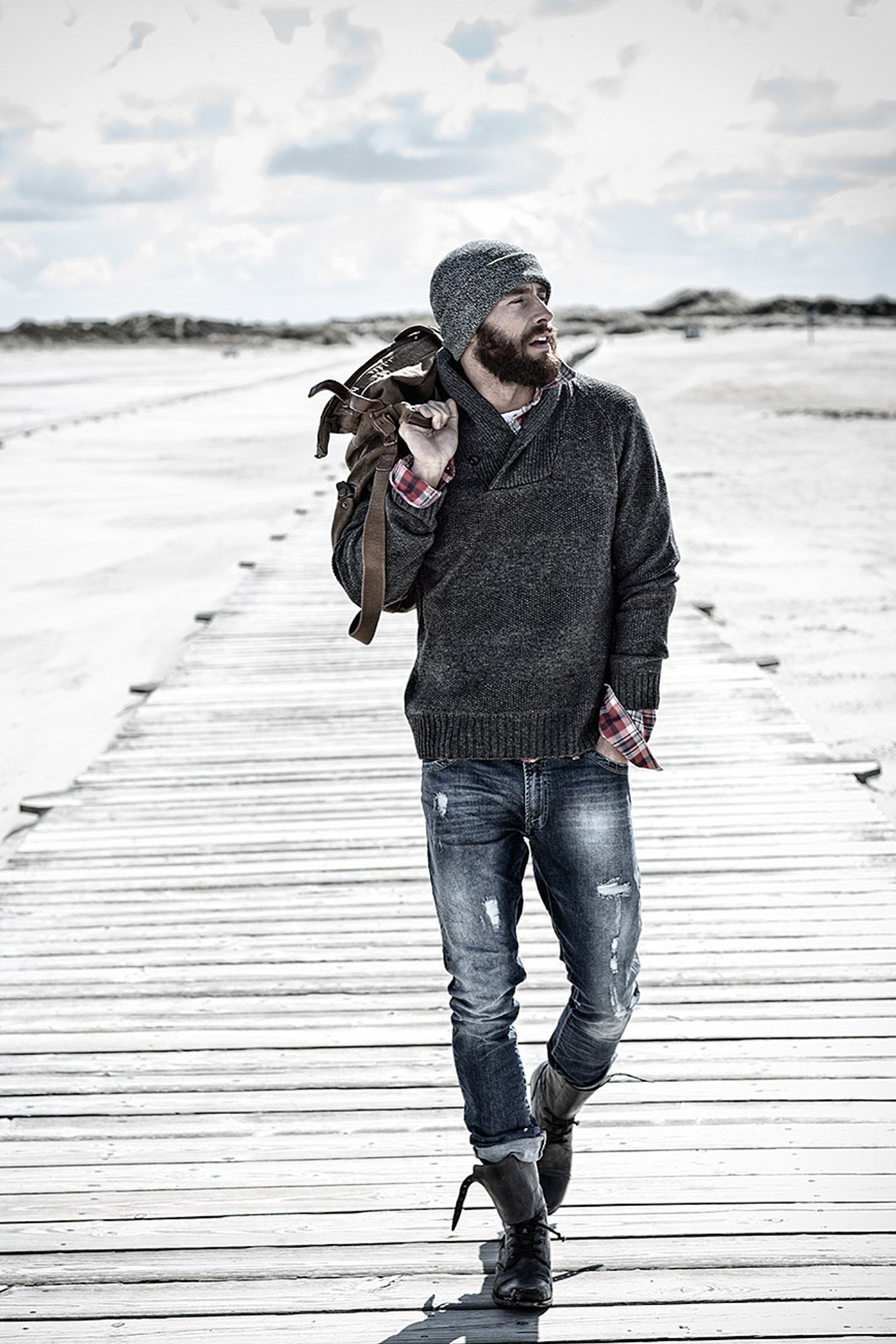 a bearded man walking on a boardwalk with a bag post production image campaign