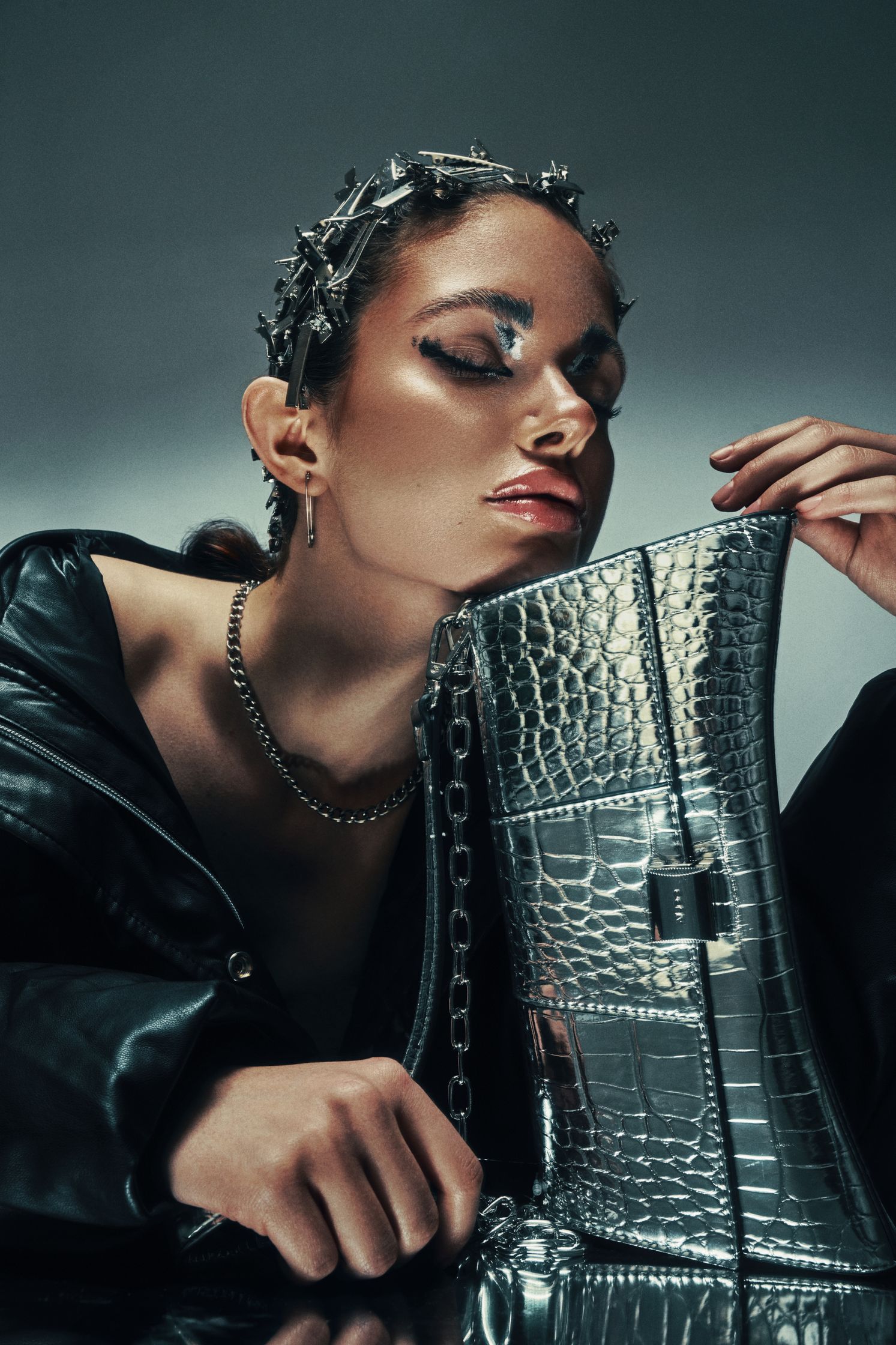 Close-up of Monique Bourscheid with metallic hair clips and dramatic silver makeup, holding a reflective handbag