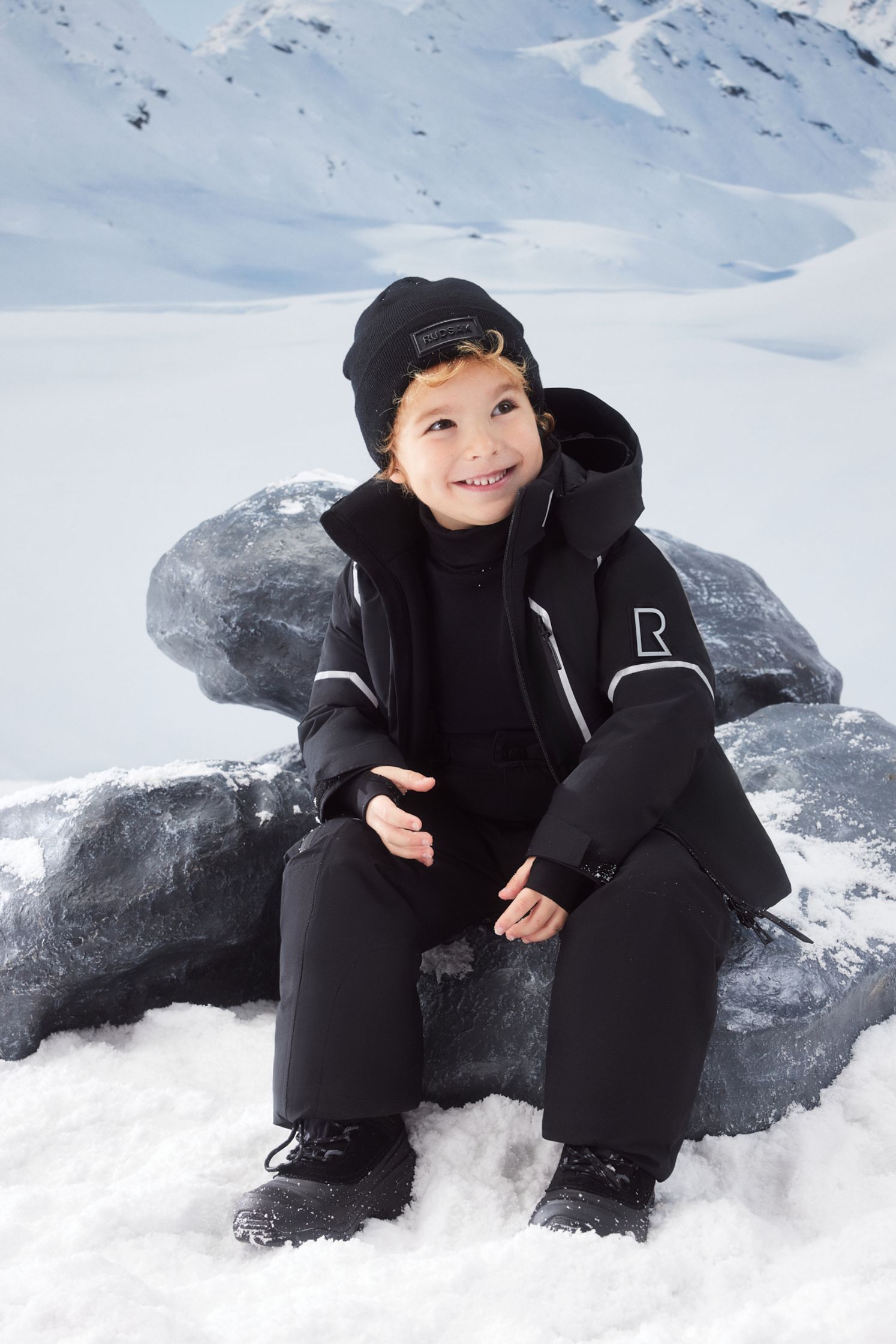 a young boy sitting on a rock in the snow