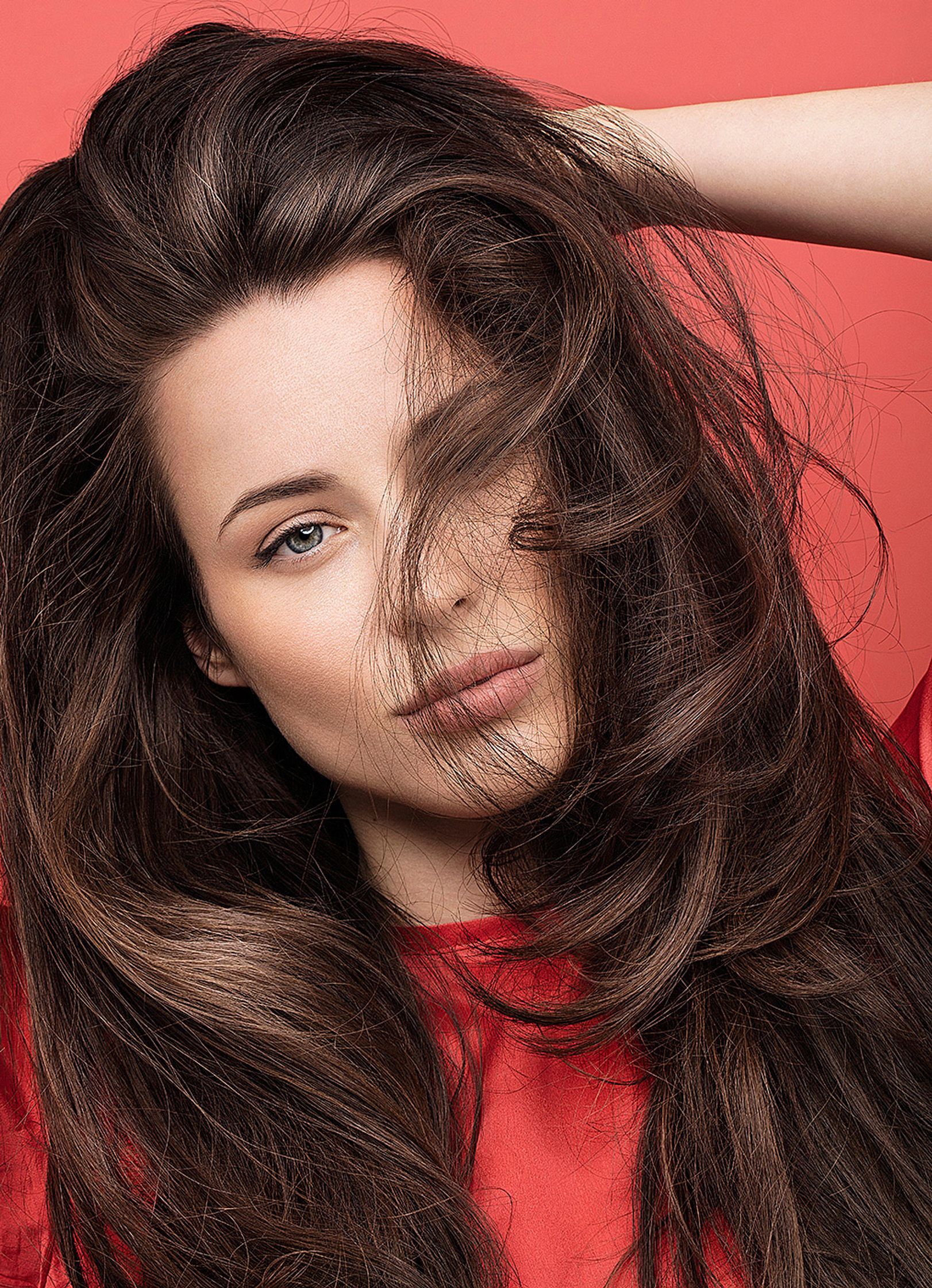 a woman with long brown hair posing on a red background retouche hamburg