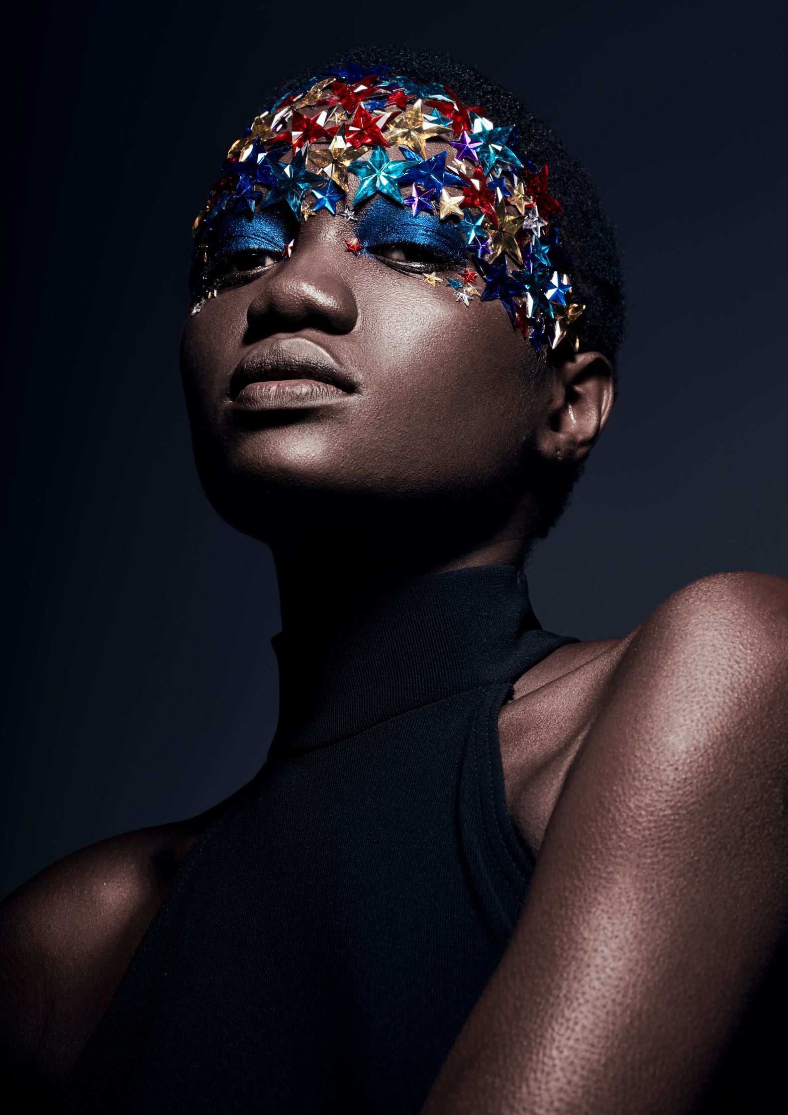 Close-up of a model with multi-colored star embellishments and blue eye makeup, portraying playful and creative beauty