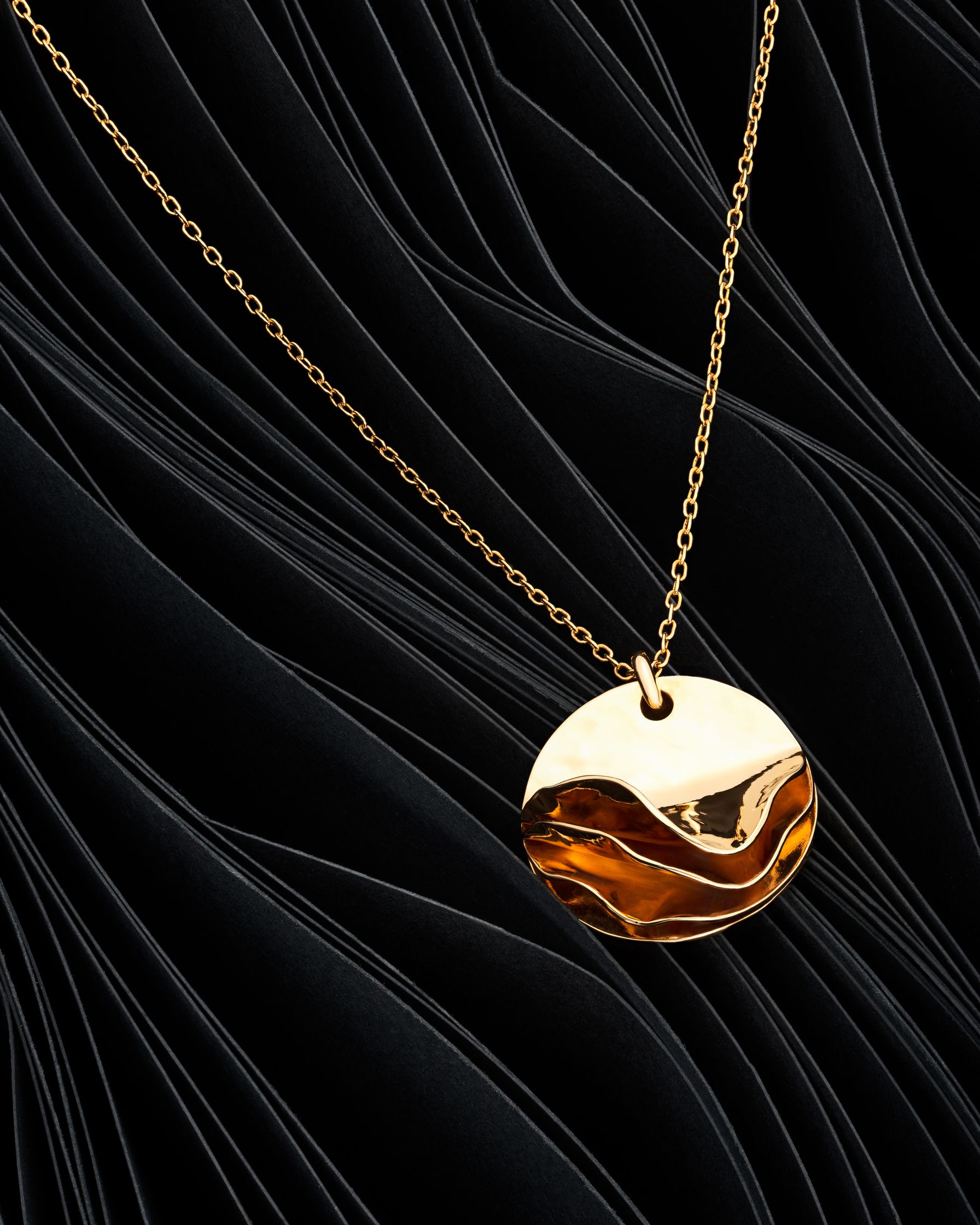 Gold pendant by Lisa Motte, suspended on black paper waves, reflecting the contrast between nature and modern design.