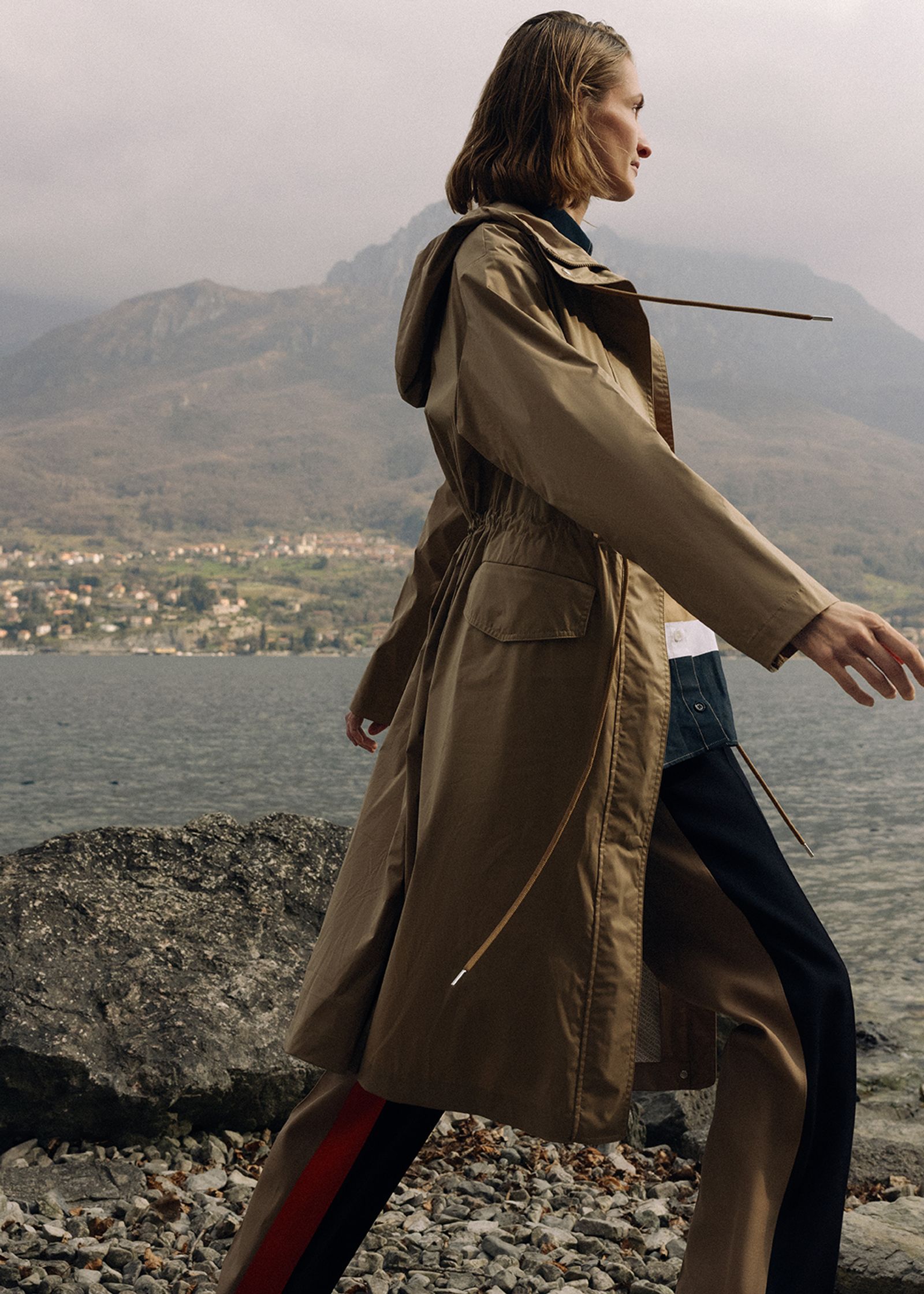 a woman in a trench coat walking on a rocky beach