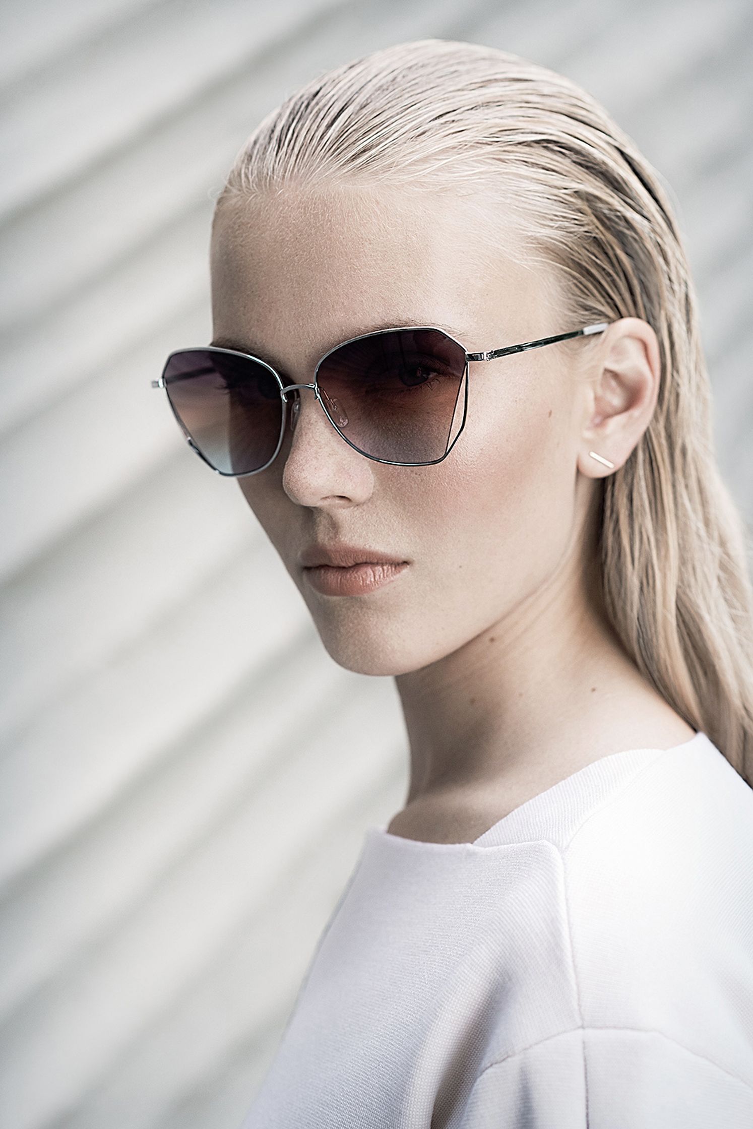 a woman wearing sunglasses in front of a white wall fashion post production