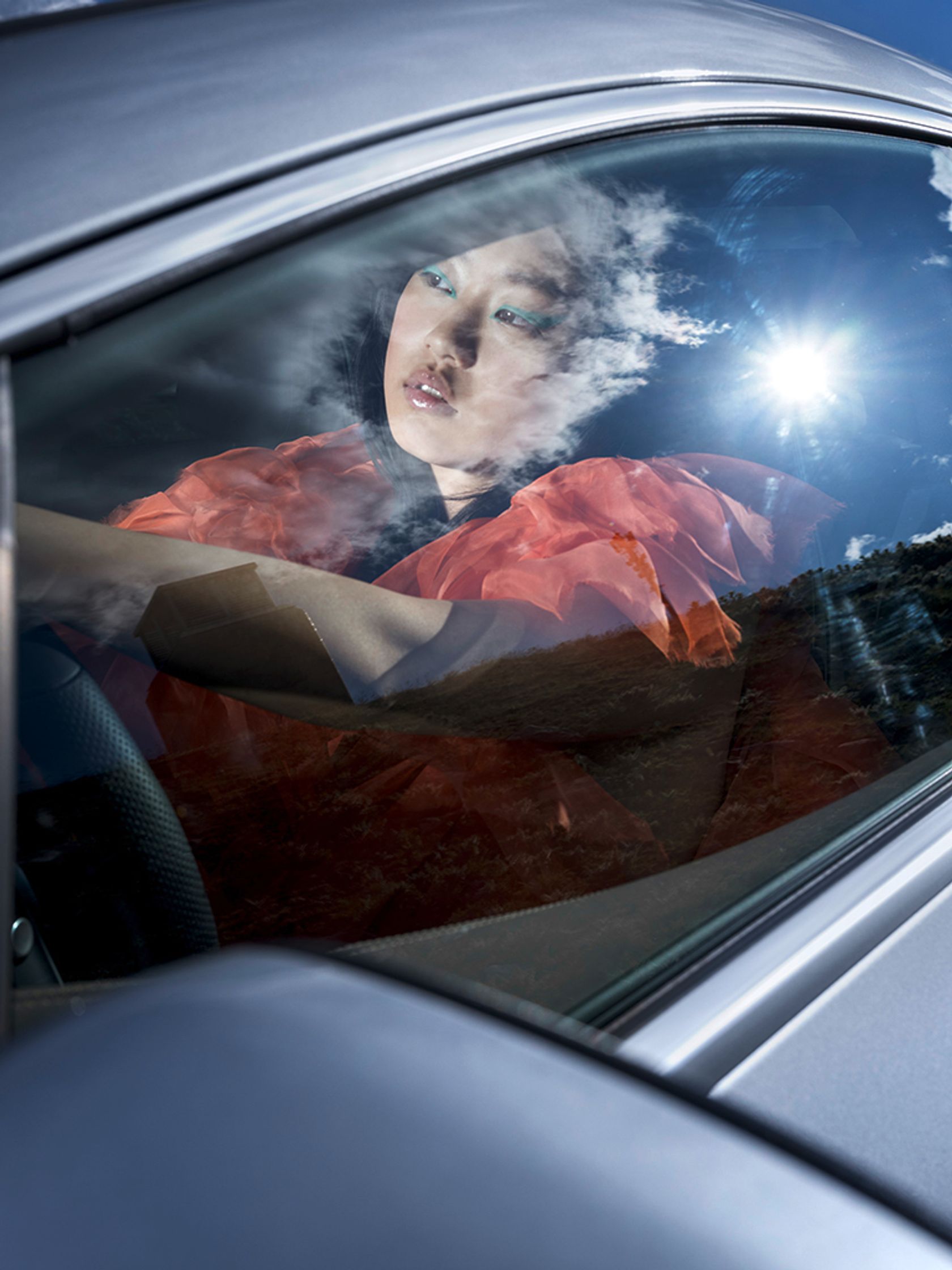 Model Dami J in a Mercedes EQE looking out the window. She wears an Amorphose orange dress. She has a turquoise graphic liner for makeup. Editorial makeup. Hair and makeup by Denise Dedich.