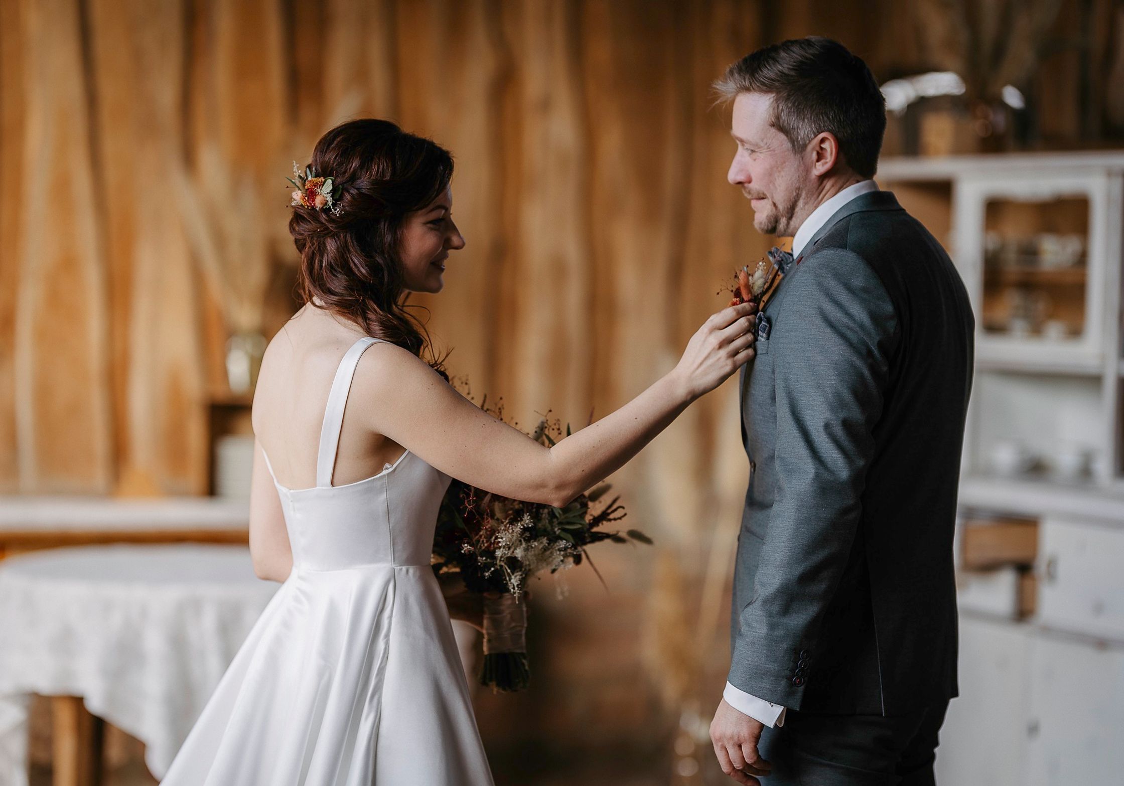 Eine Braut und ein Bräutigam, die in einer rustikalen Scheune ihre Hochzeitskrawatten anziehen