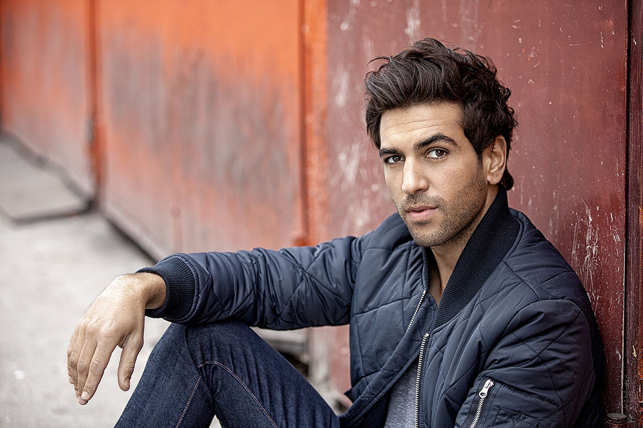 elyas m'barek in a blue jacket leaning against a wall
retusche by glamtouch