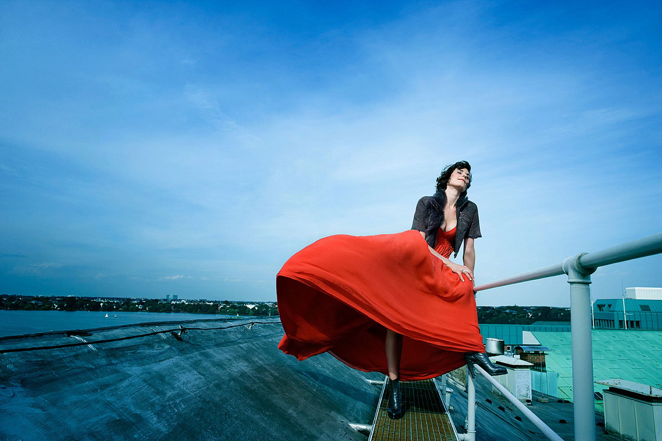 a woman in a red dress standing on a railing editorial fashion retusche