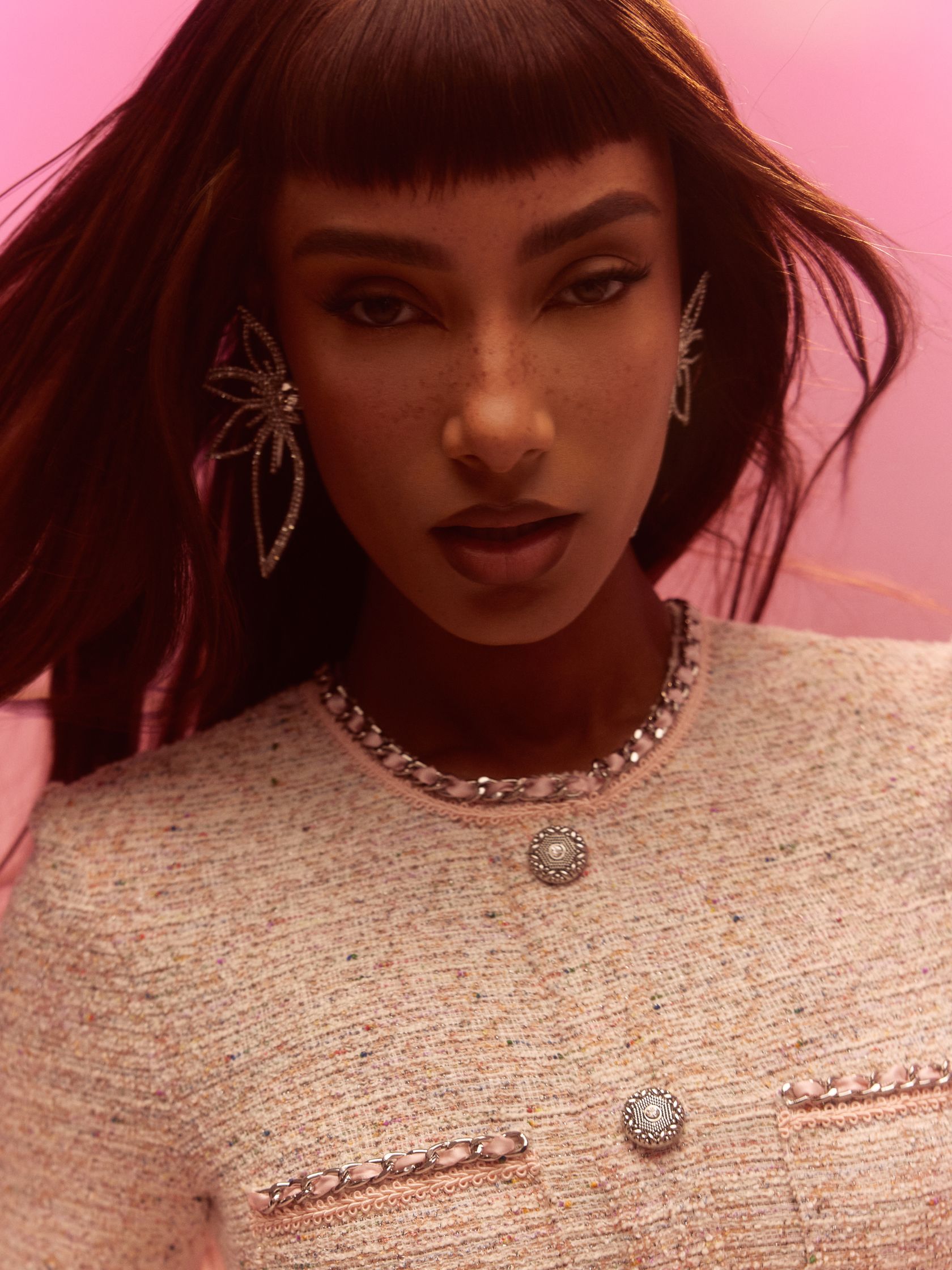 a black woman in a tweed jacket posing in front of a pink background