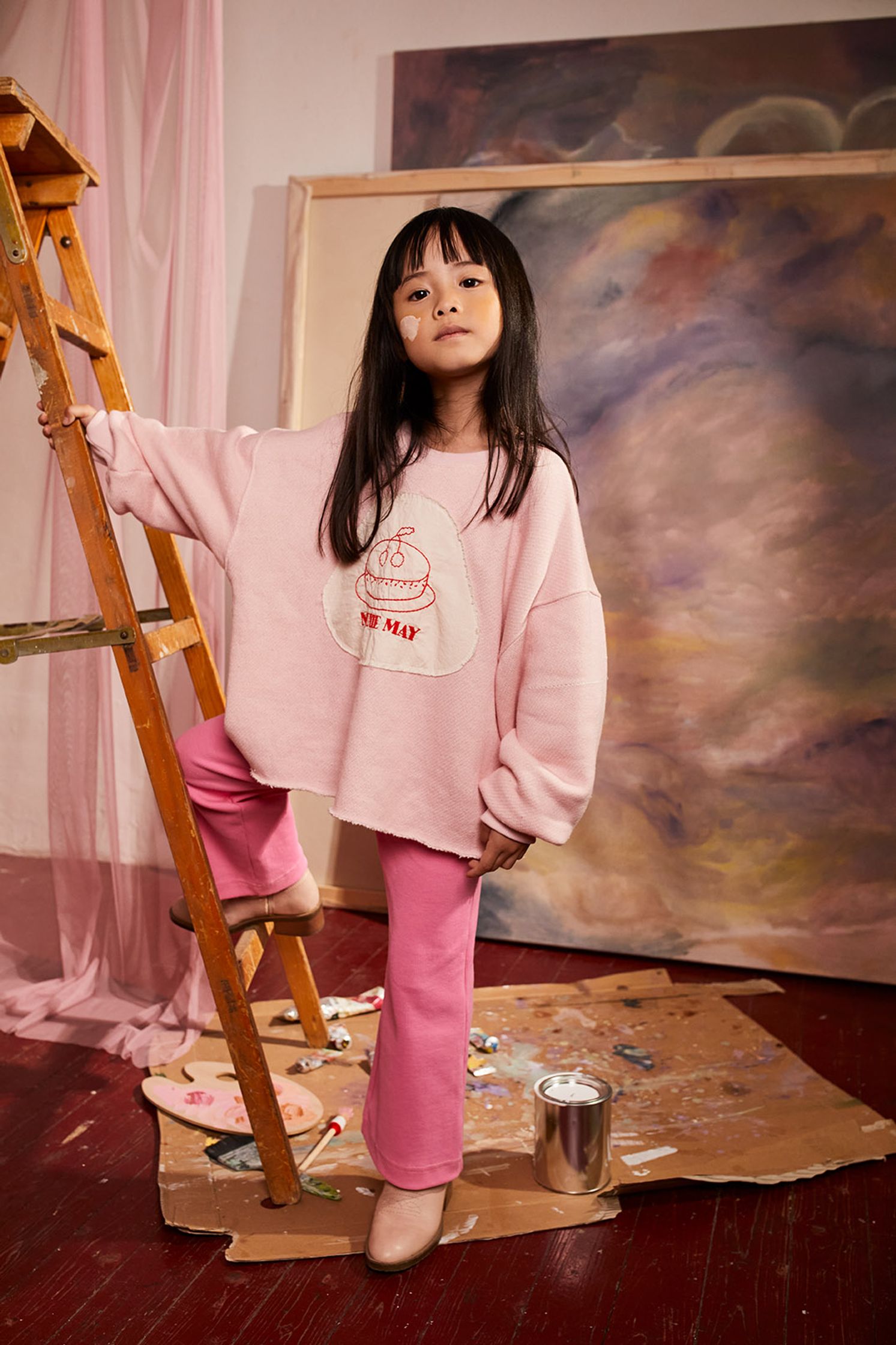 a little girl standing on a ladder in front of a painting