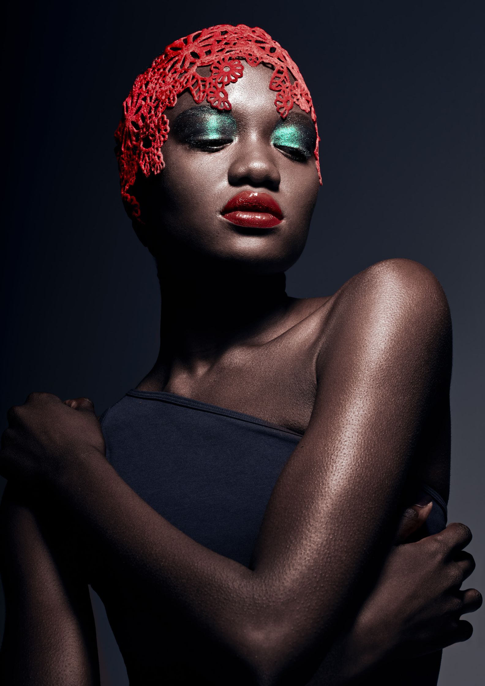 Beauty portrait of a model with vibrant red lace headpiece and striking green eye makeup, exuding elegance and confidence