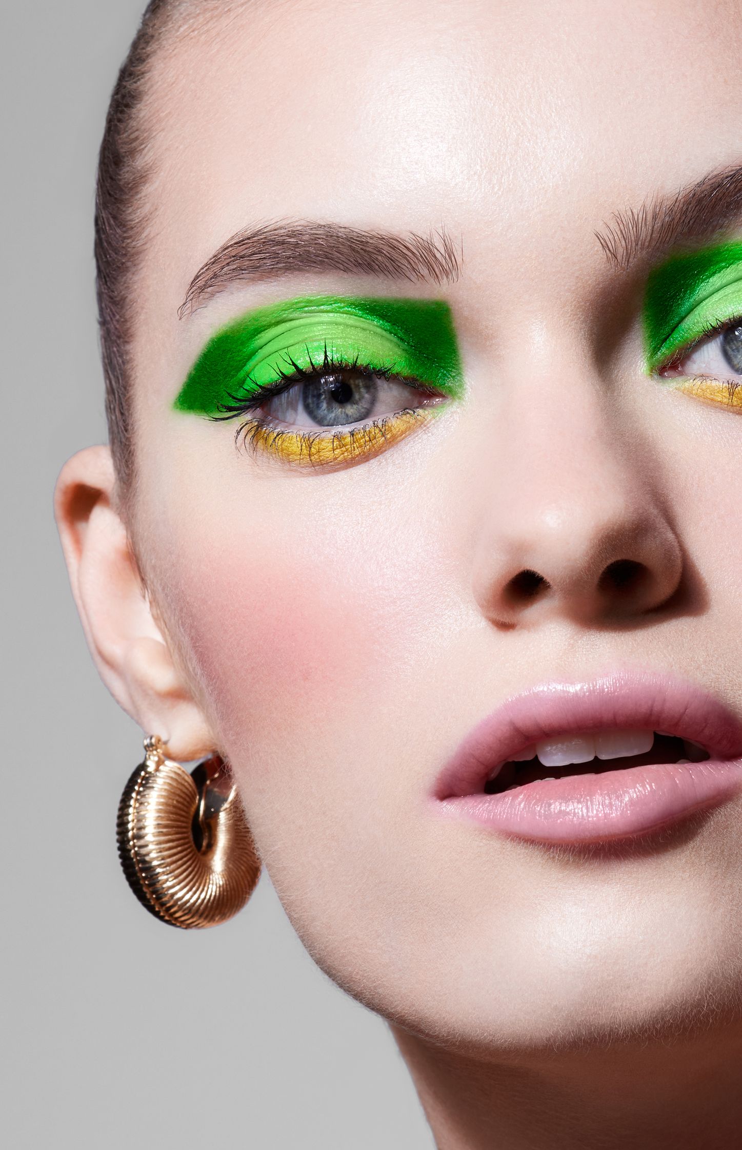 a woman with green eye makeup and gold earrings