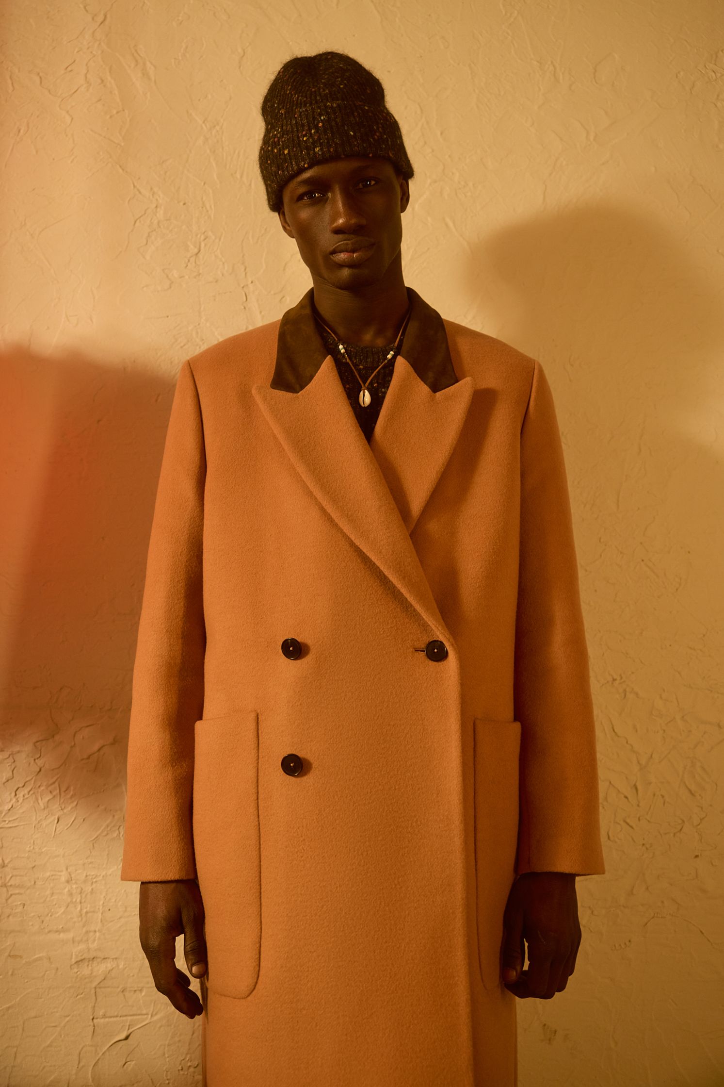 a man in an orange coat standing in front of a wall