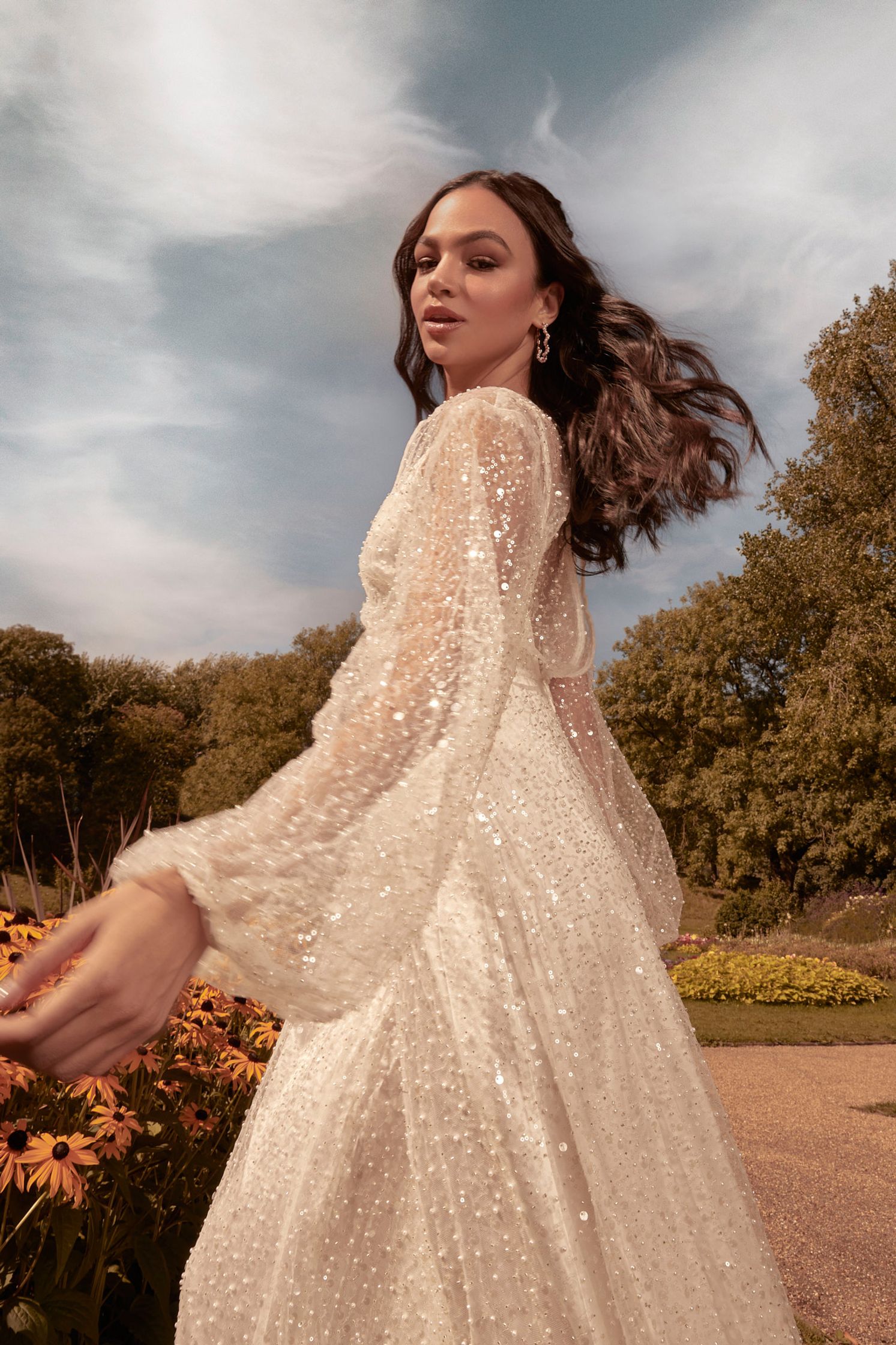 a woman in a white dress is walking through a garden