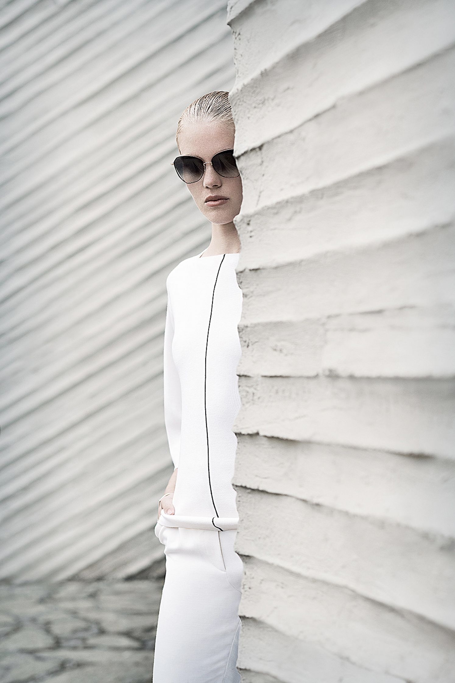 a woman in a white outfit leaning against a wall fashion post production