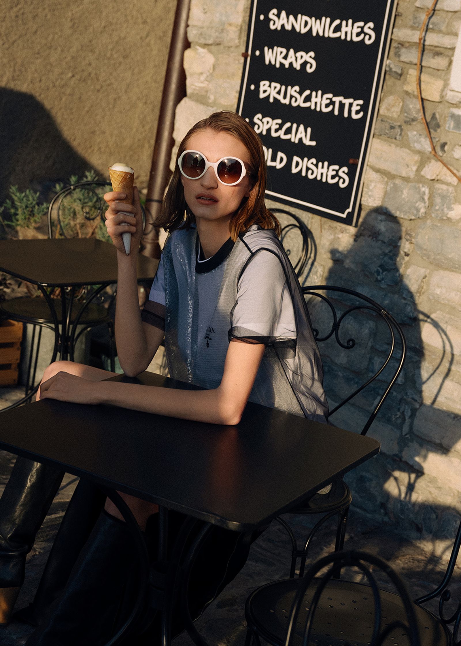 a woman sitting at a table eating an ice cream cone