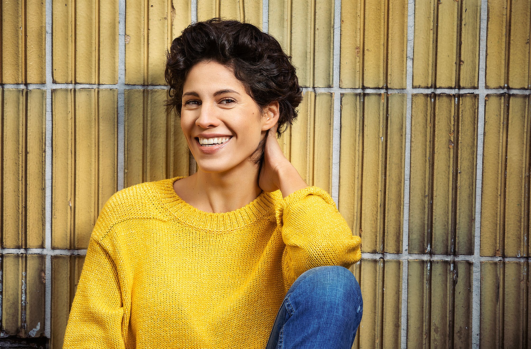 a smiling jasmin gerat in a yellow sweater leaning against a wall
retouche by glamtouch