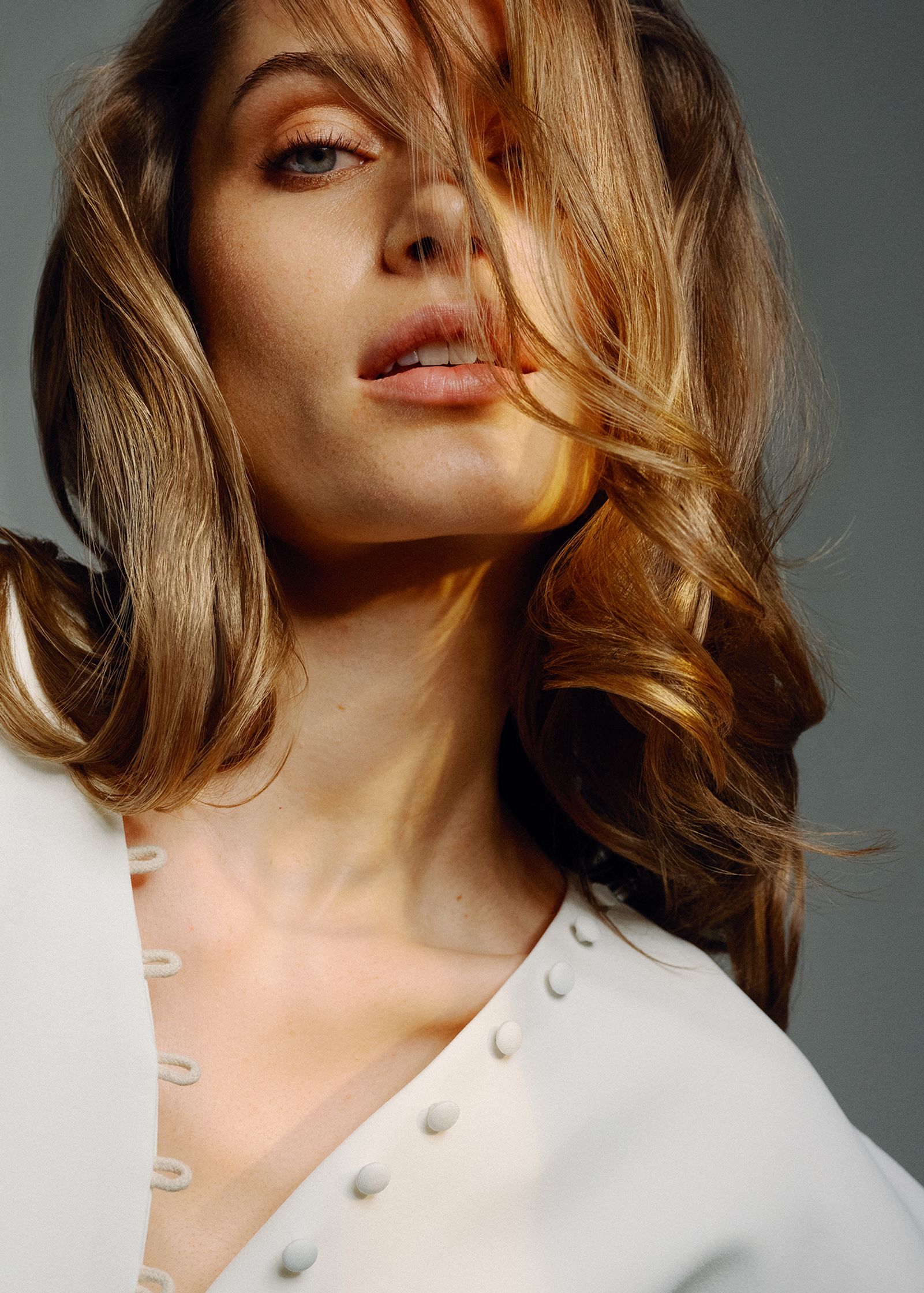 a woman in a white top posing with her hair blowing in the wind