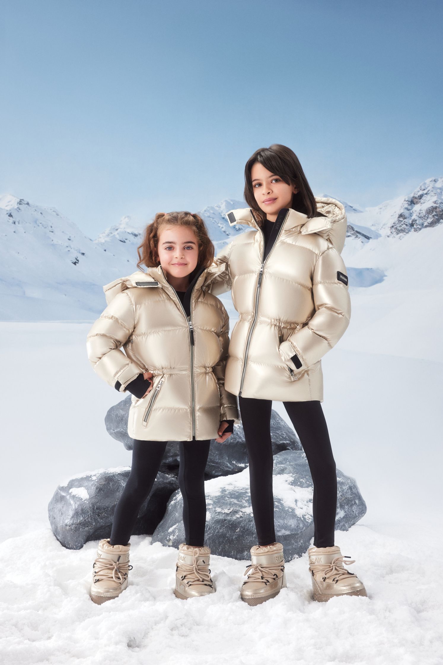 two girls standing in the snow wearing down jackets